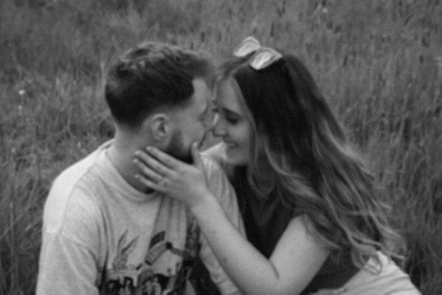 A romantic black and white portrait of a couple sharing an intimate moment in tall grass.