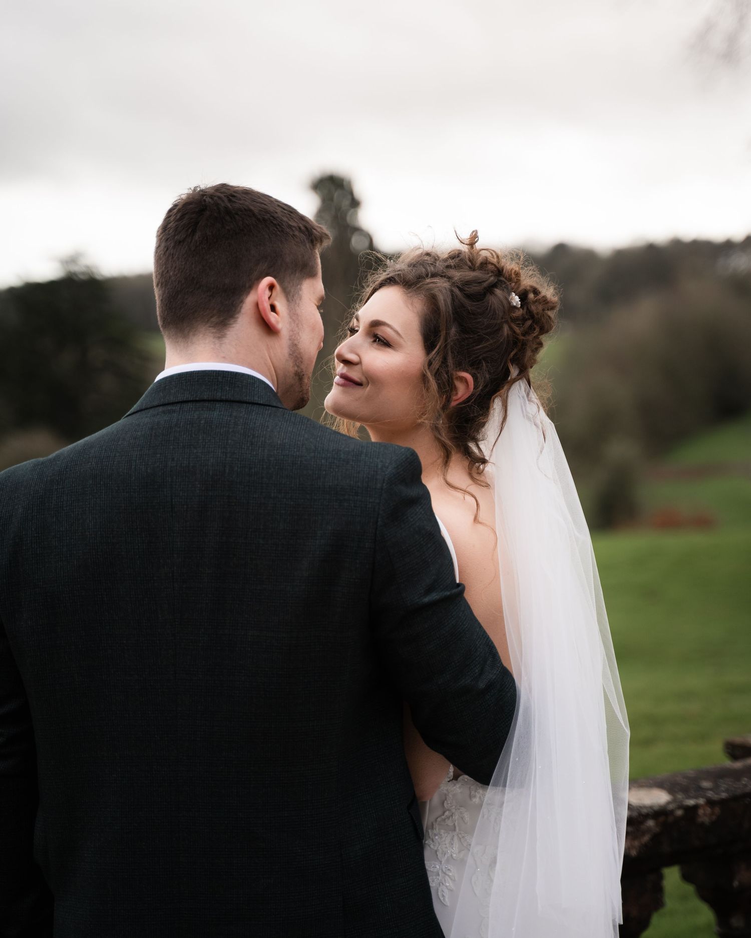A romantic wedding moment captured outdoors with the bride in a white gown and veil looking lovingly at her groom.