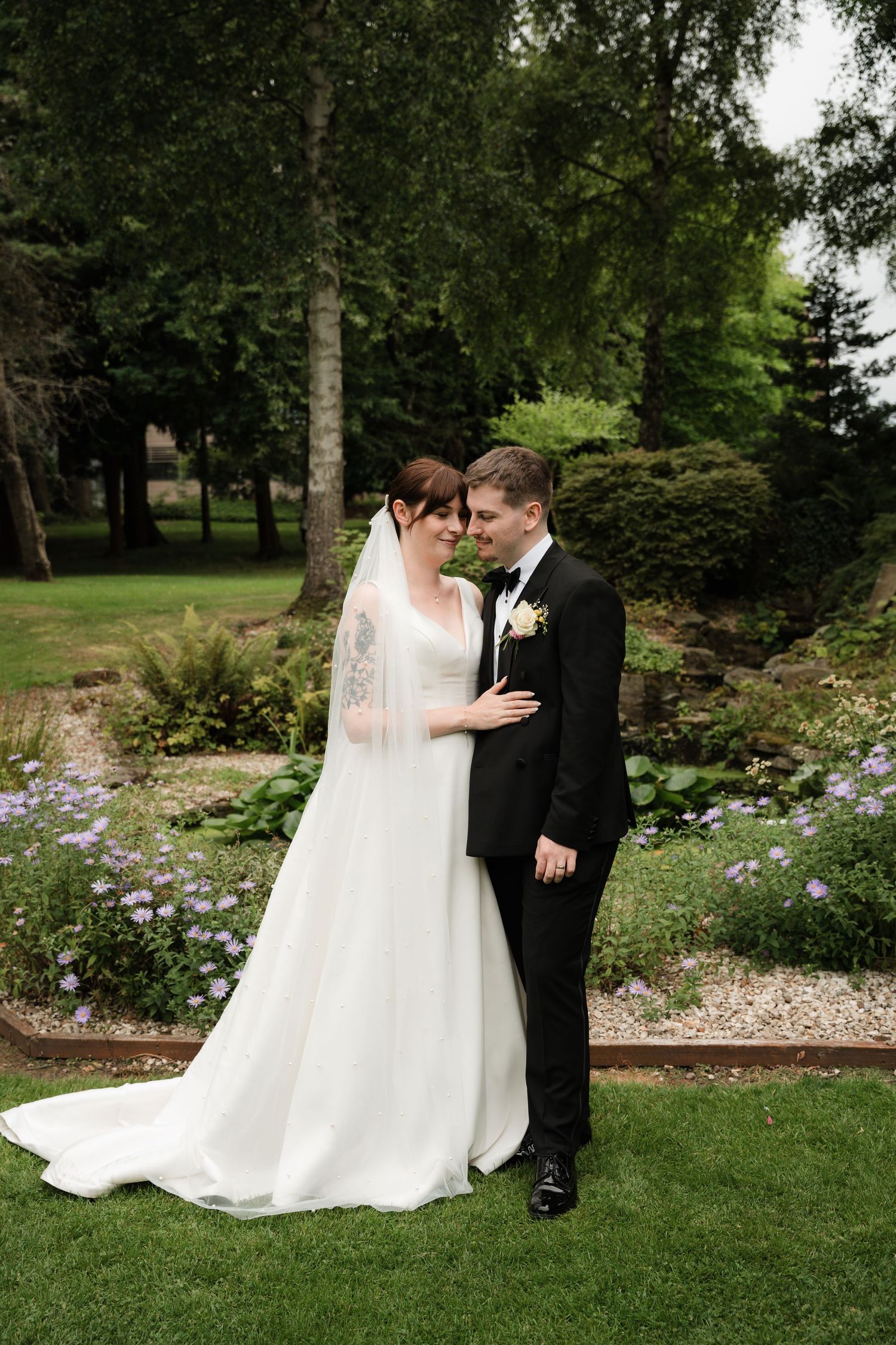 A couple in wedding attire share an intimate moment together in a lush garden setting with blooming flowers.