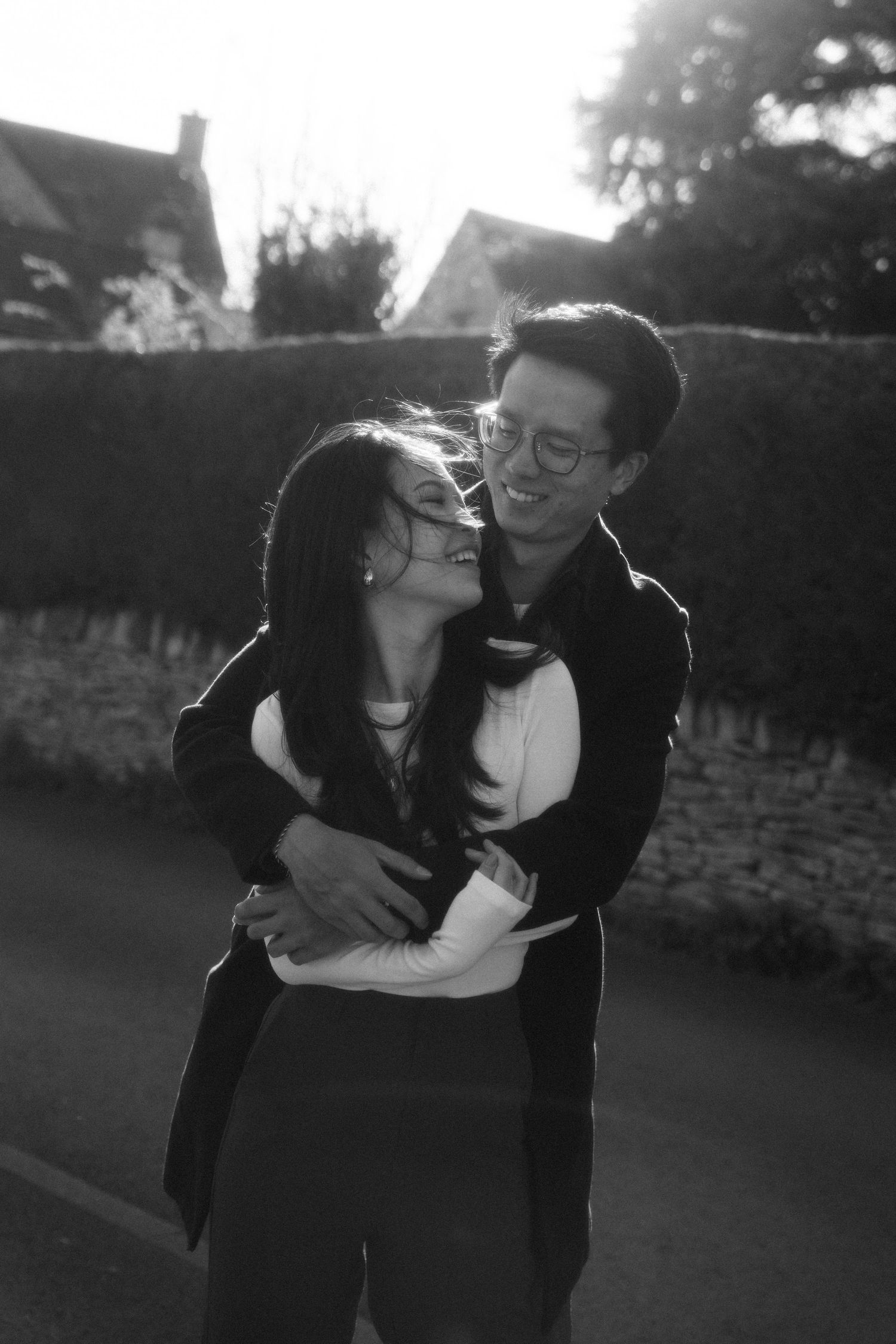 Black and white photo of couple laughing and embracing against stone wall.