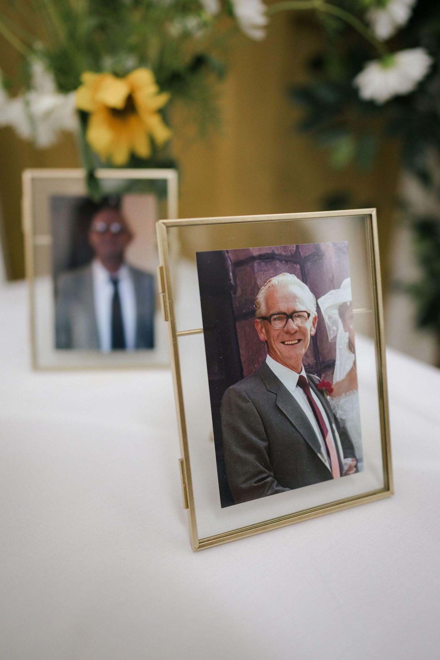 Framed photographs displayed on a white surface with yellow flowers visible in soft focus.