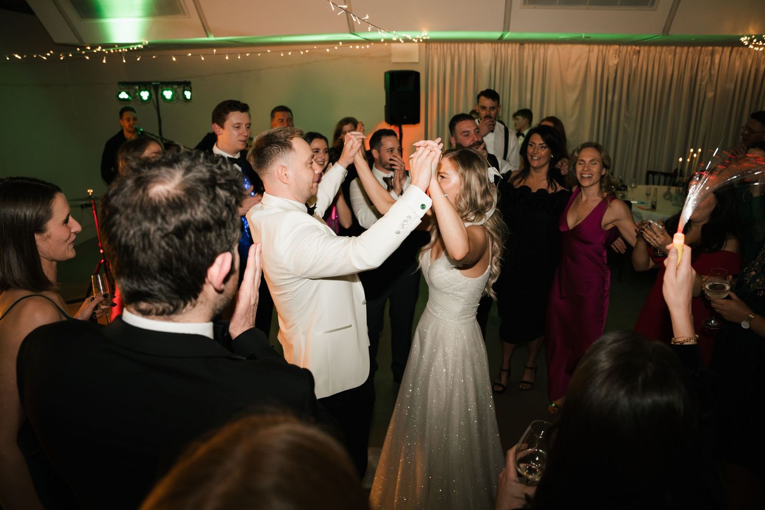 Wedding reception guests dancing and celebrating on the dance floor under green lighting at an evening party.