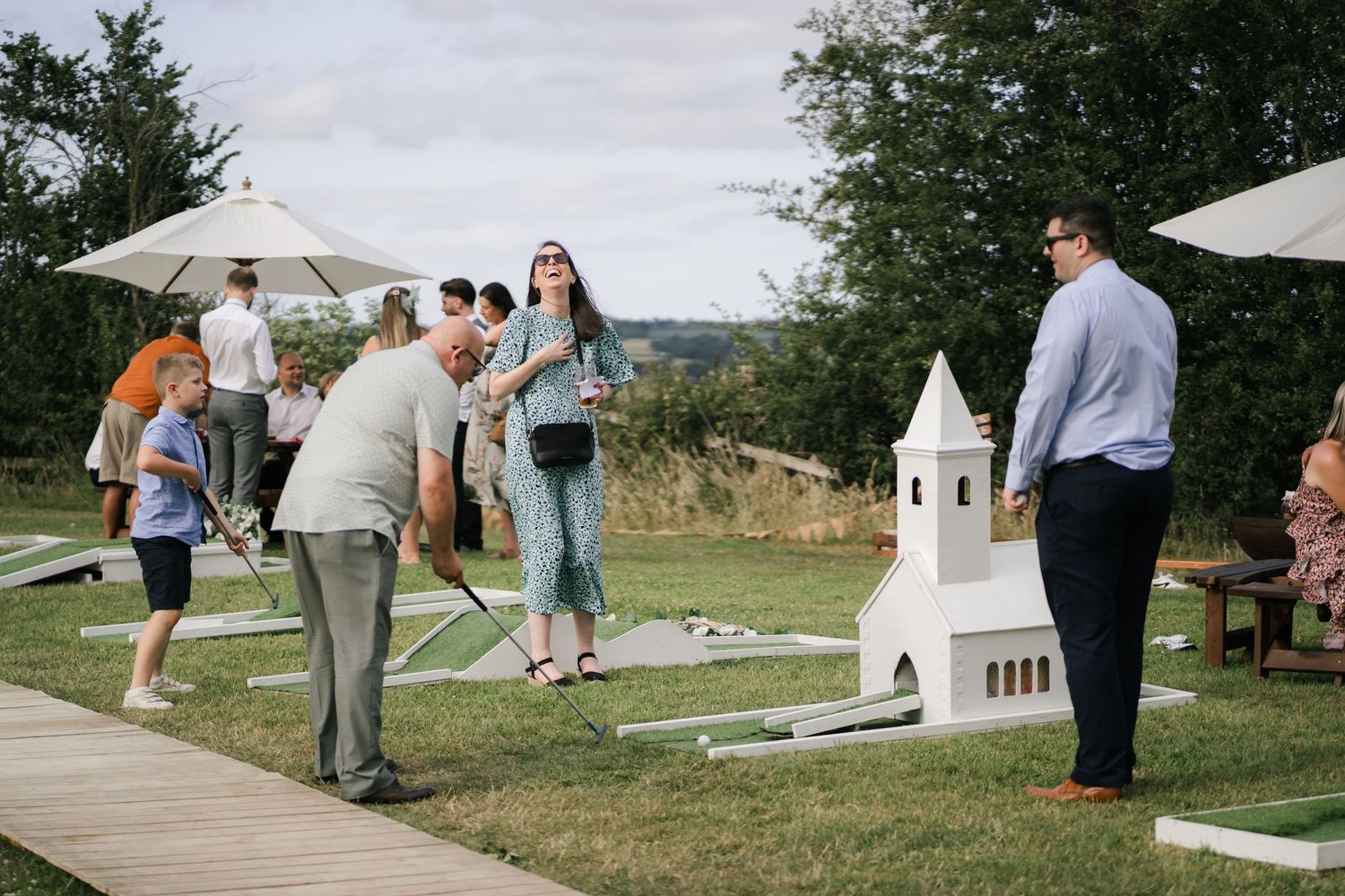Wedding guests gather outdoors on a sunny day around white tents and decorations during a celebration.