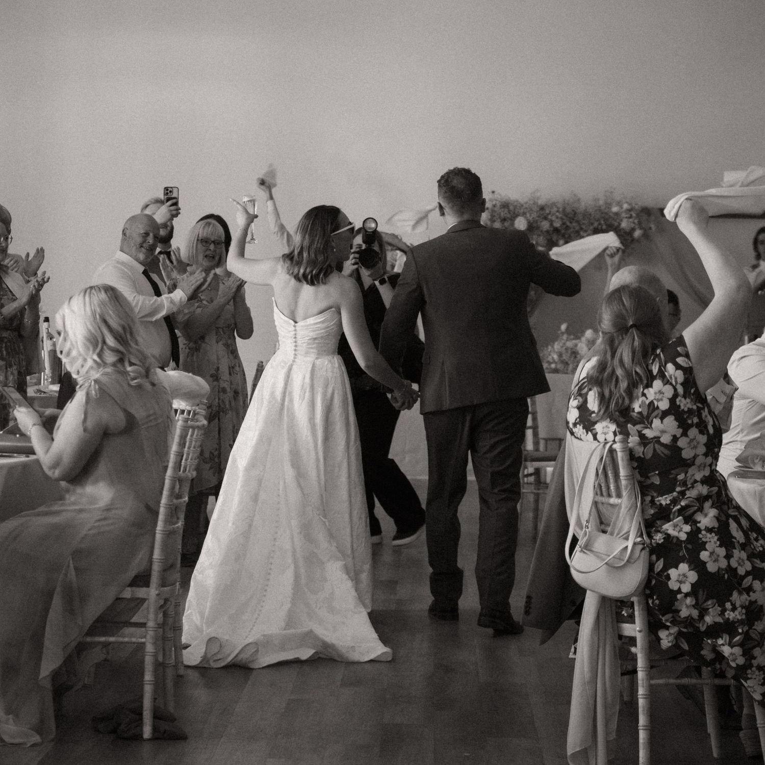 Black and white panoramic photo showing couples dancing at a wedding reception in an elegant venue.