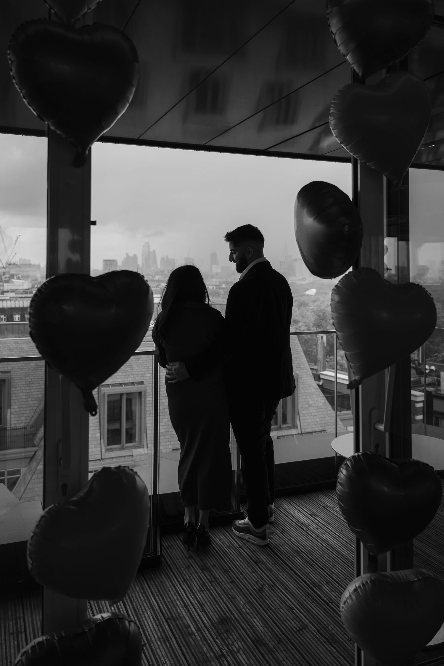 Silhouetted figures stand in a dimly lit room with large windows overlooking a cityscape.