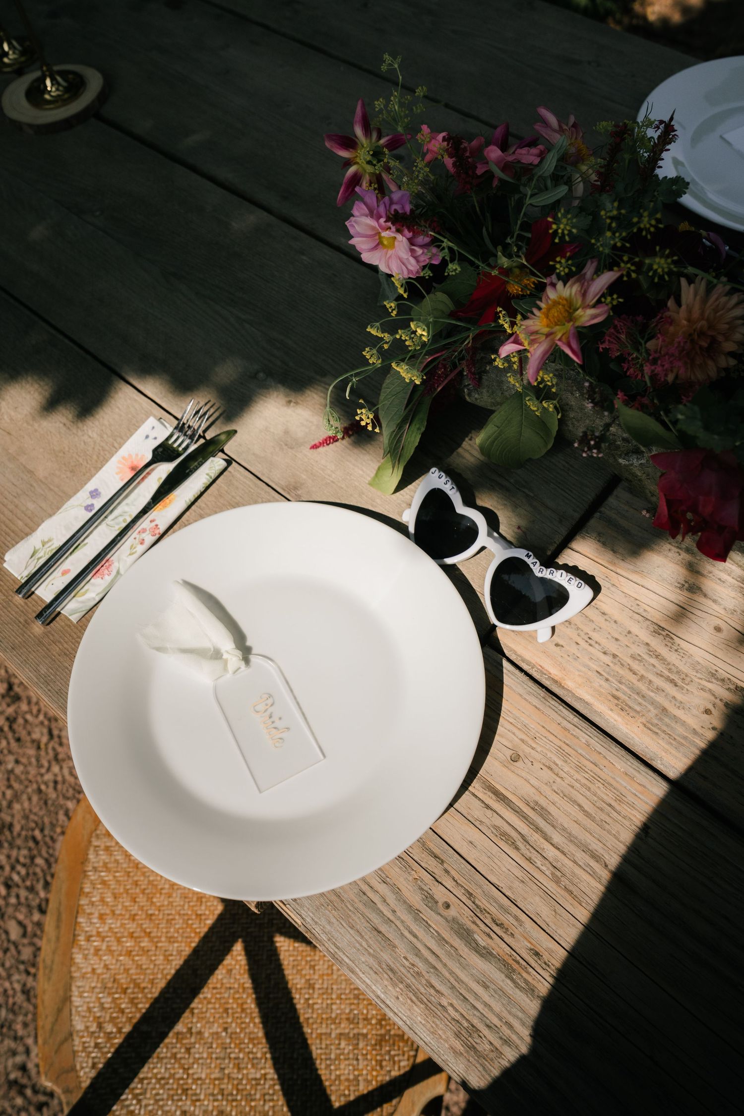 Artistic progression of empty white plates with silverware and flowers on a rustic wooden table in natural lighting.