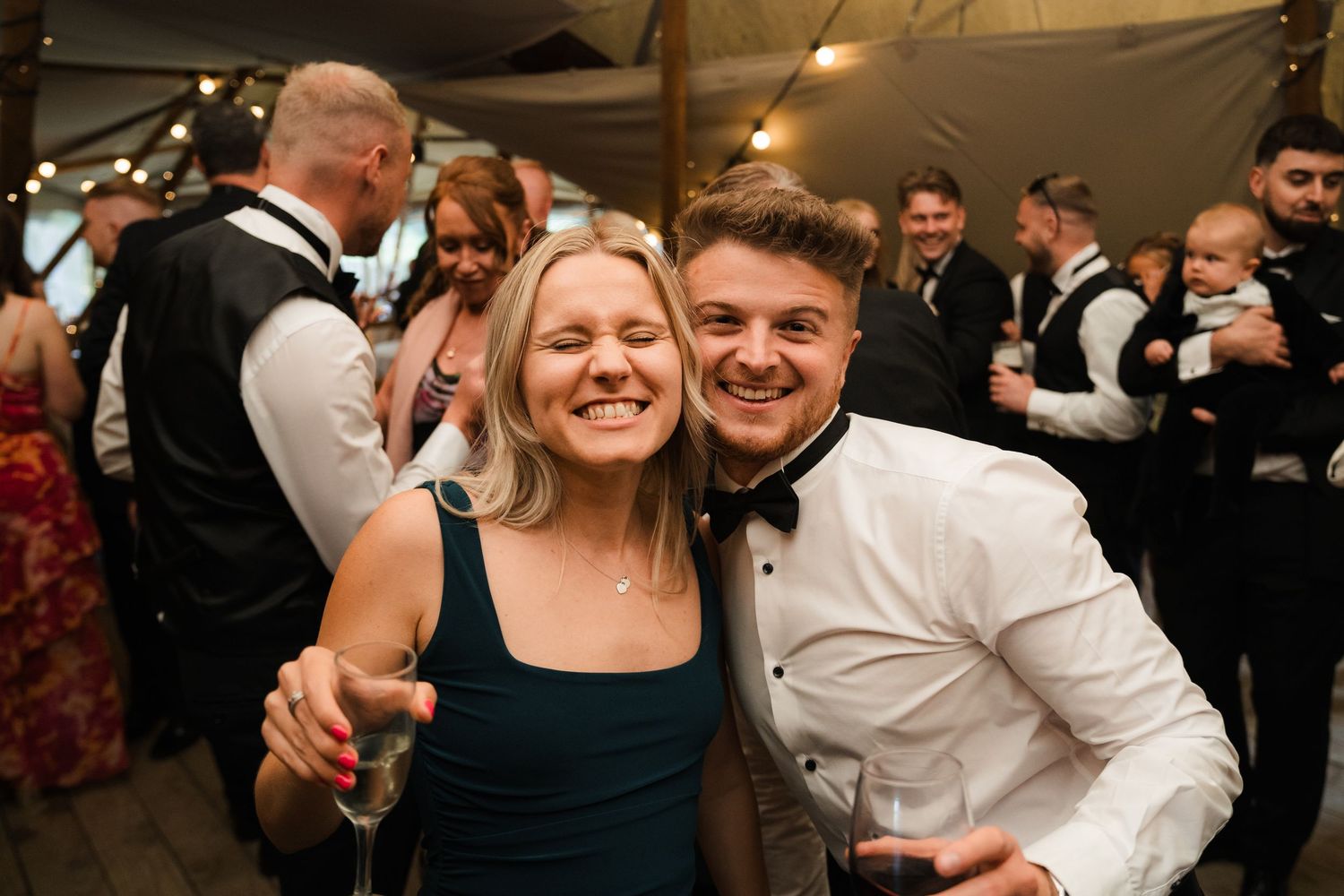 Wedding guests smile and celebrate on the dance floor during a joyful reception party.