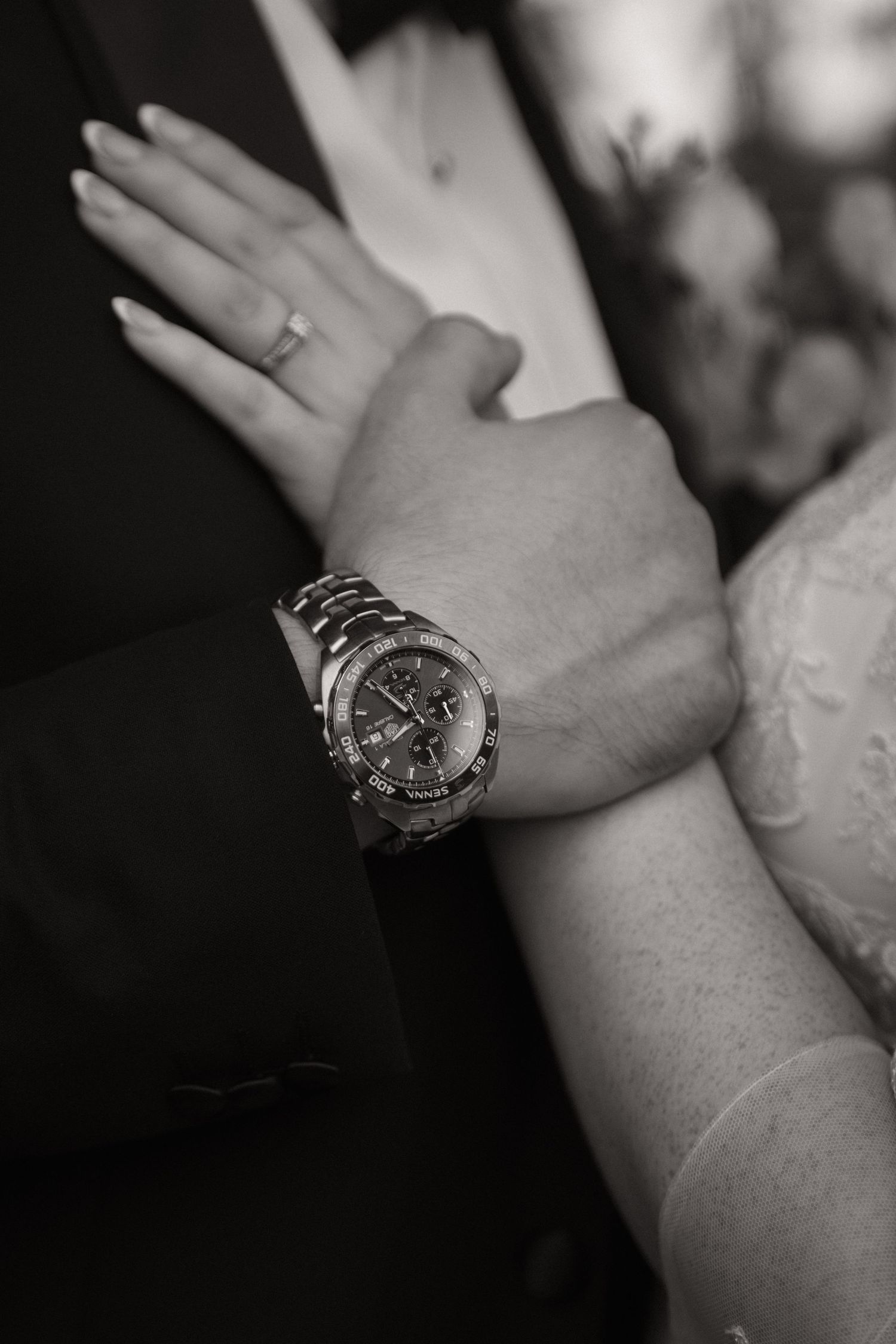Close-up black and white photo of hands with elegant watch and wedding rings.