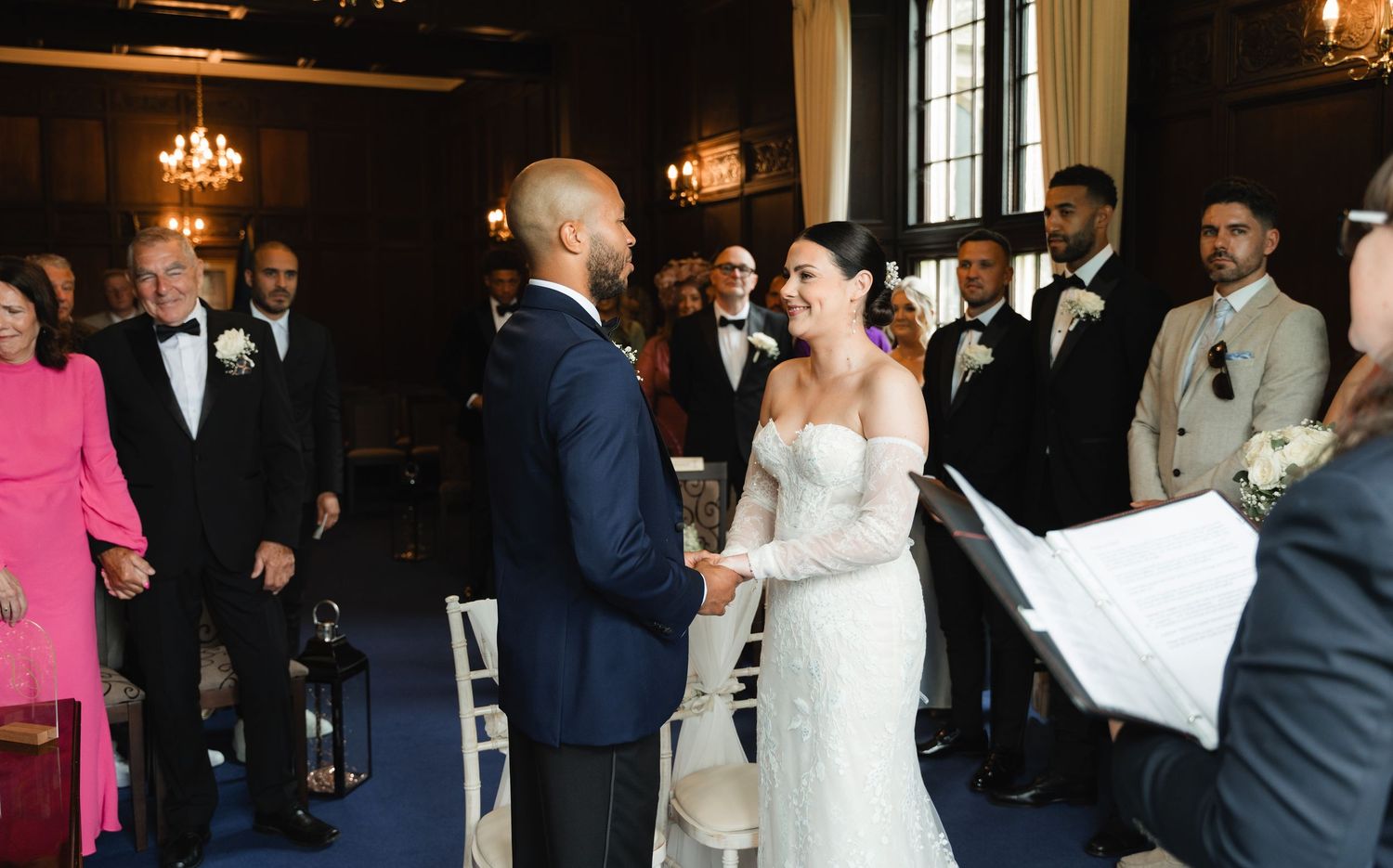 A wedding ceremony in progress with guests watching as the couple exchanges vows in an elegant indoor venue.