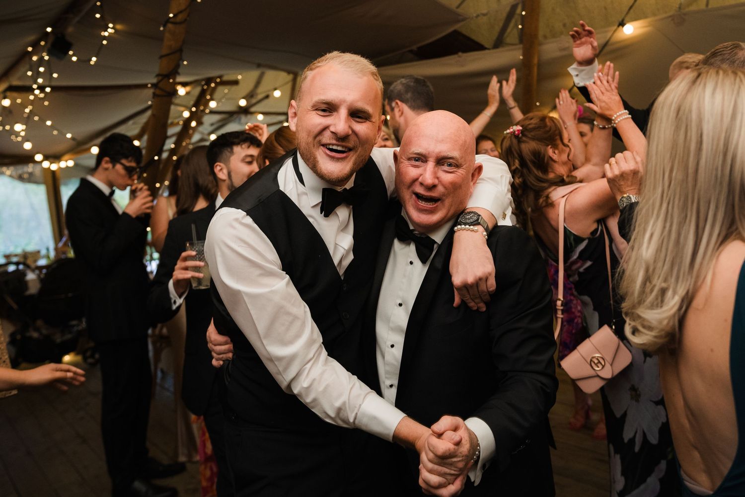 Wedding guests dancing and celebrating on the dance floor under twinkling lights at an evening reception.