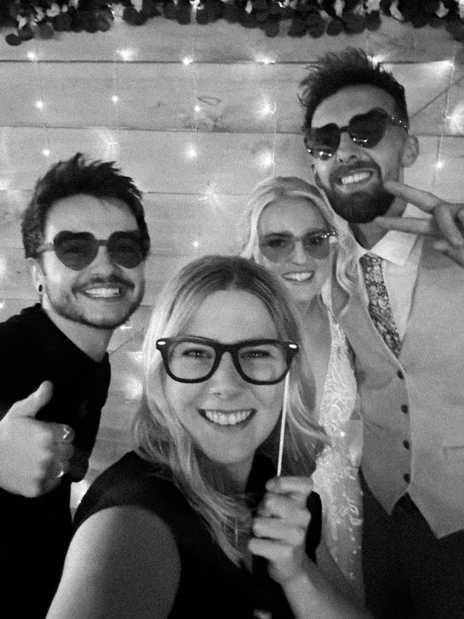A series of black and white selfies showing a group of friends smiling together with string lights in the background.