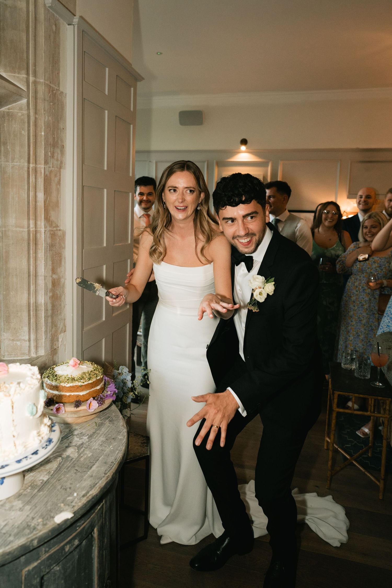 Newlyweds dance together at their wedding reception in an elegant venue with guests looking on.