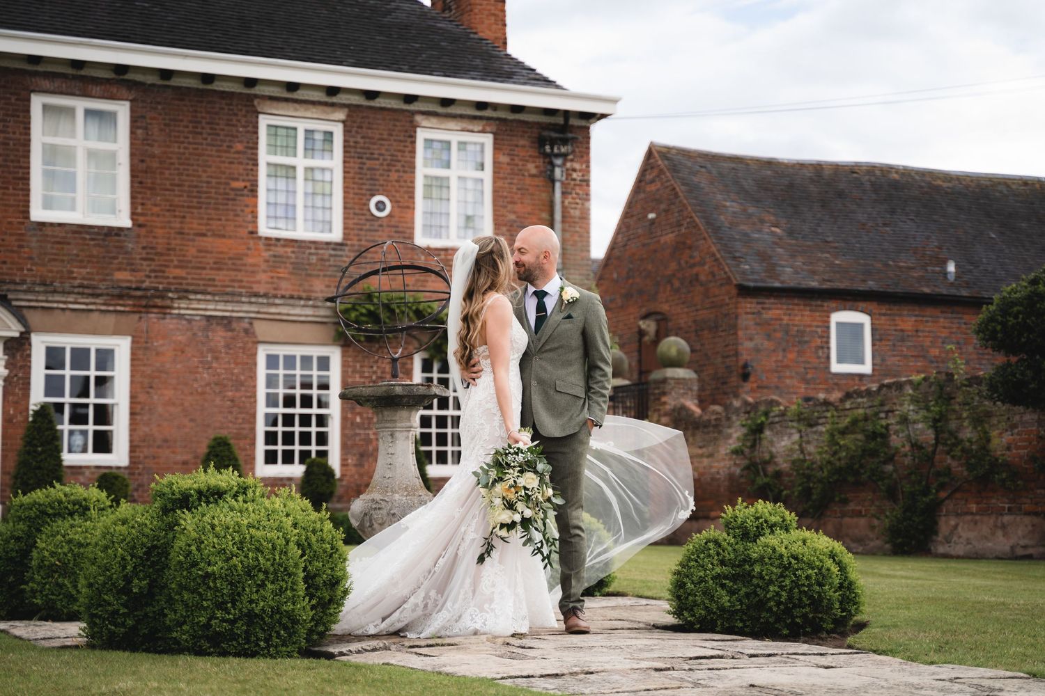 A bride and groom share romantic moments in front of a traditional brick English manor house.