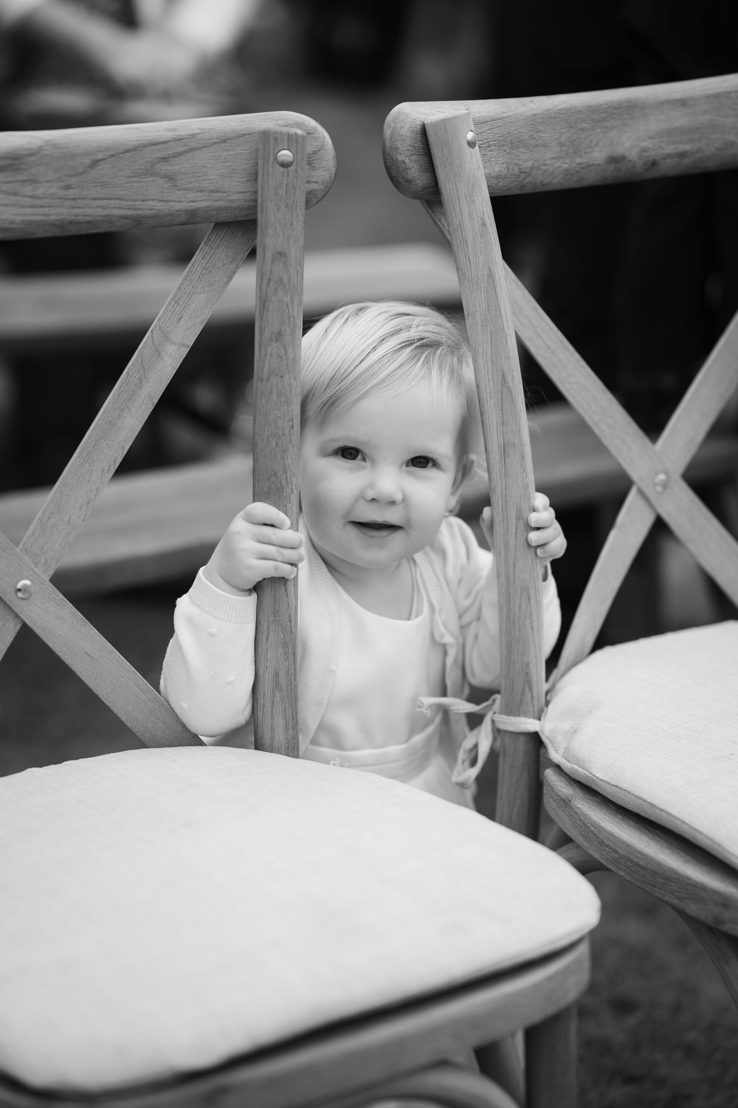 Black and white series of a baby peeking through wooden chair slats while sitting in a dining chair.