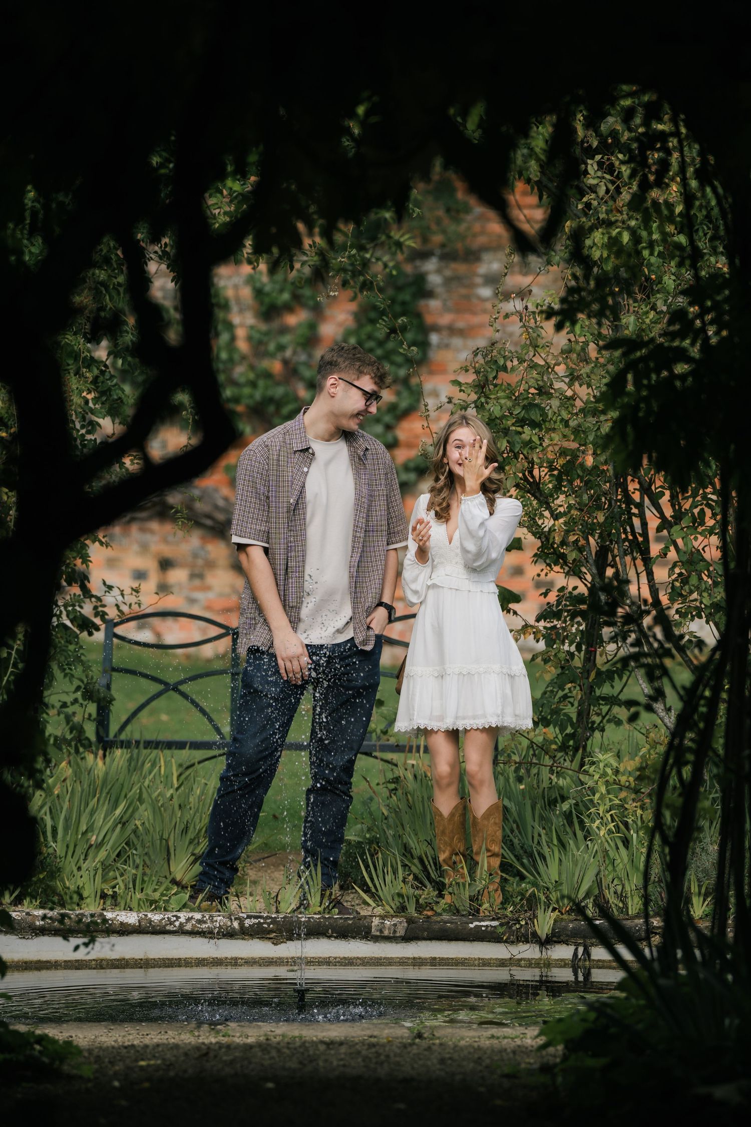 A couple shares a romantic moment together in a garden setting with natural sunlight filtering through trees.