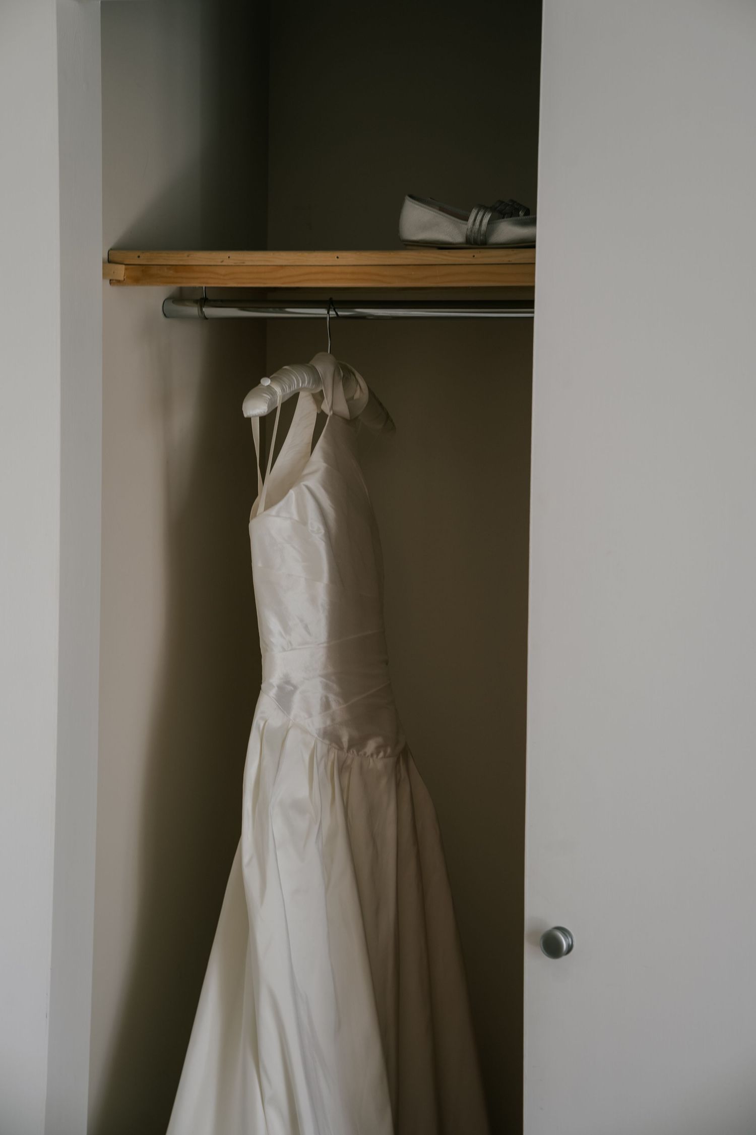 White wedding dress hanging in a closet with wooden shelving visible in the background.