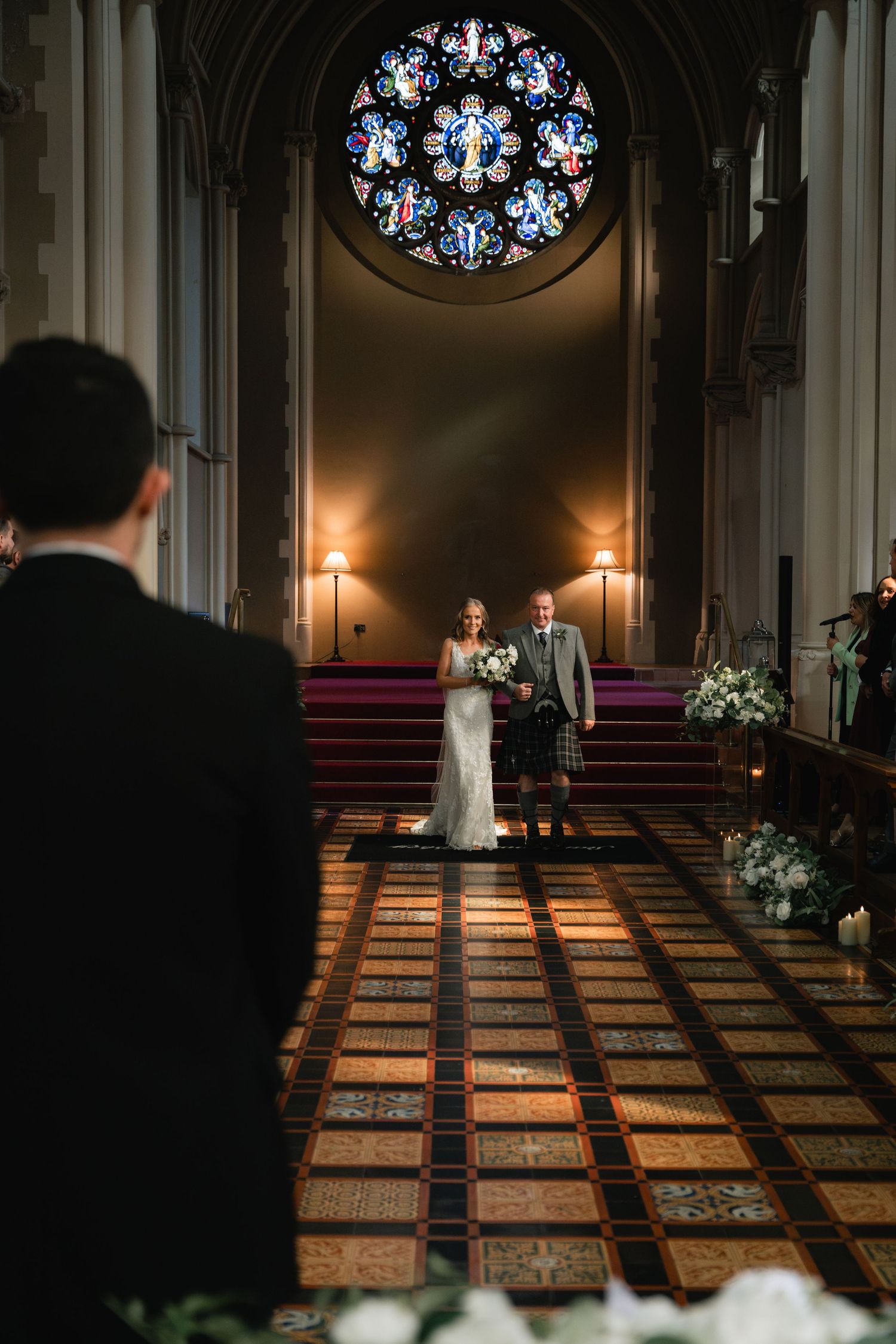 Elegant wedding ceremony inside historic church with ornate tiled floors and stained glass windows illuminated by candlelight.