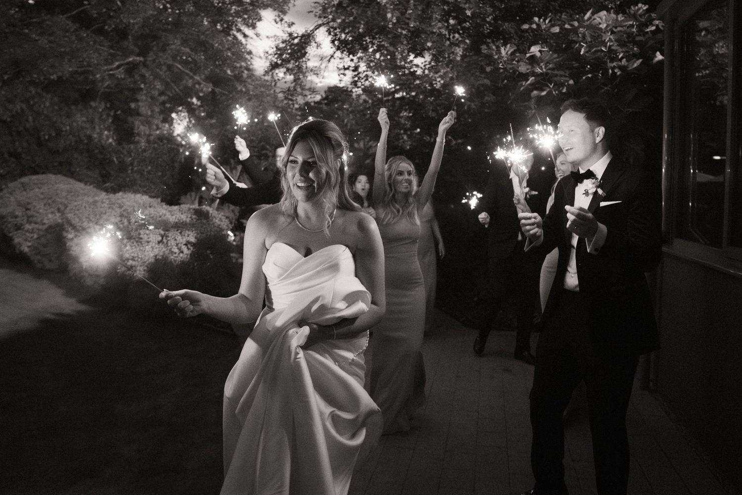 A black and white wedding celebration at night with sparklers creating a magical illuminated walkway.