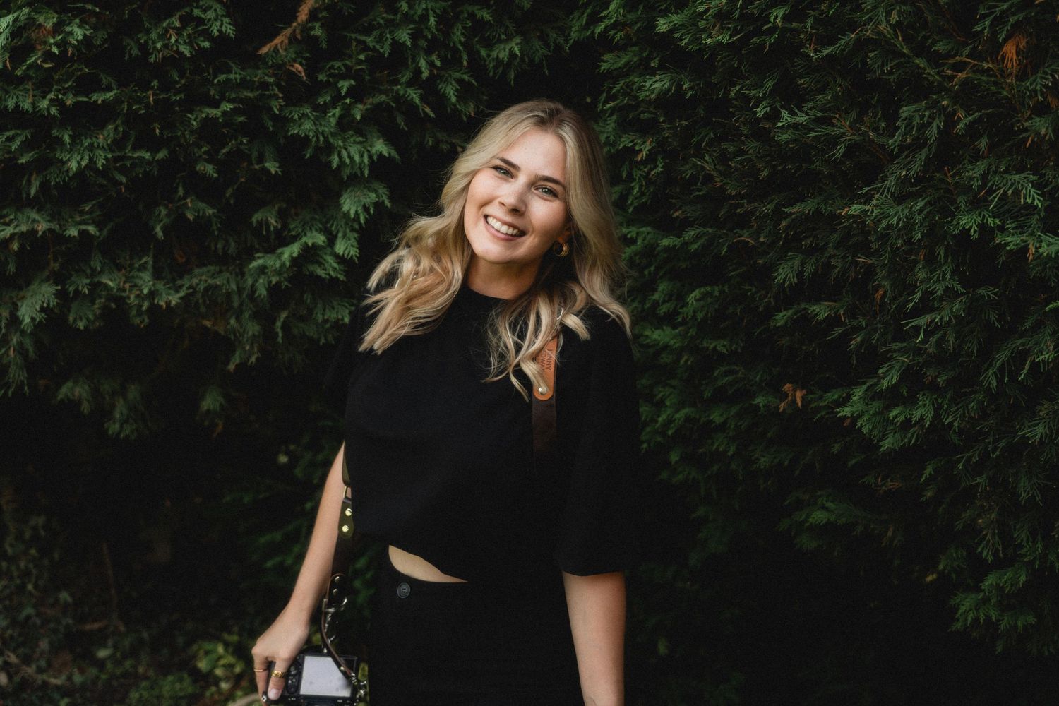 Casual outdoor portrait session against lush green hedge background.