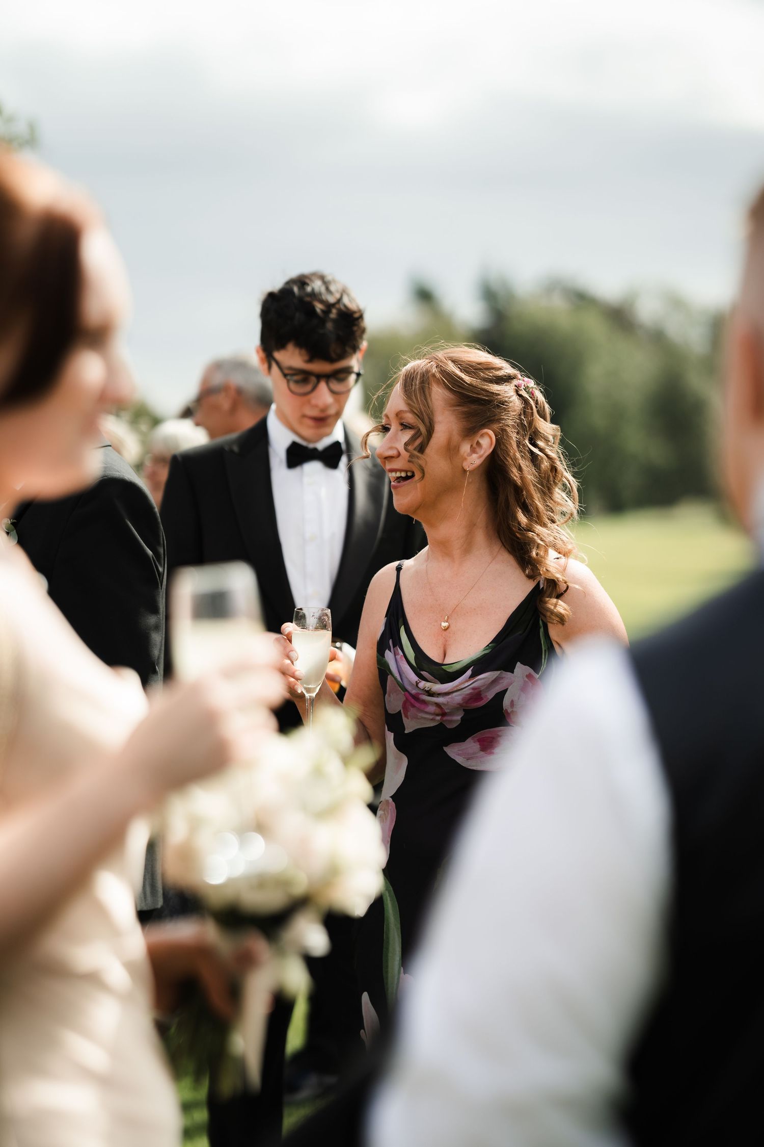 Guests mingle at an elegant outdoor wedding reception with formal attire and champagne glasses.