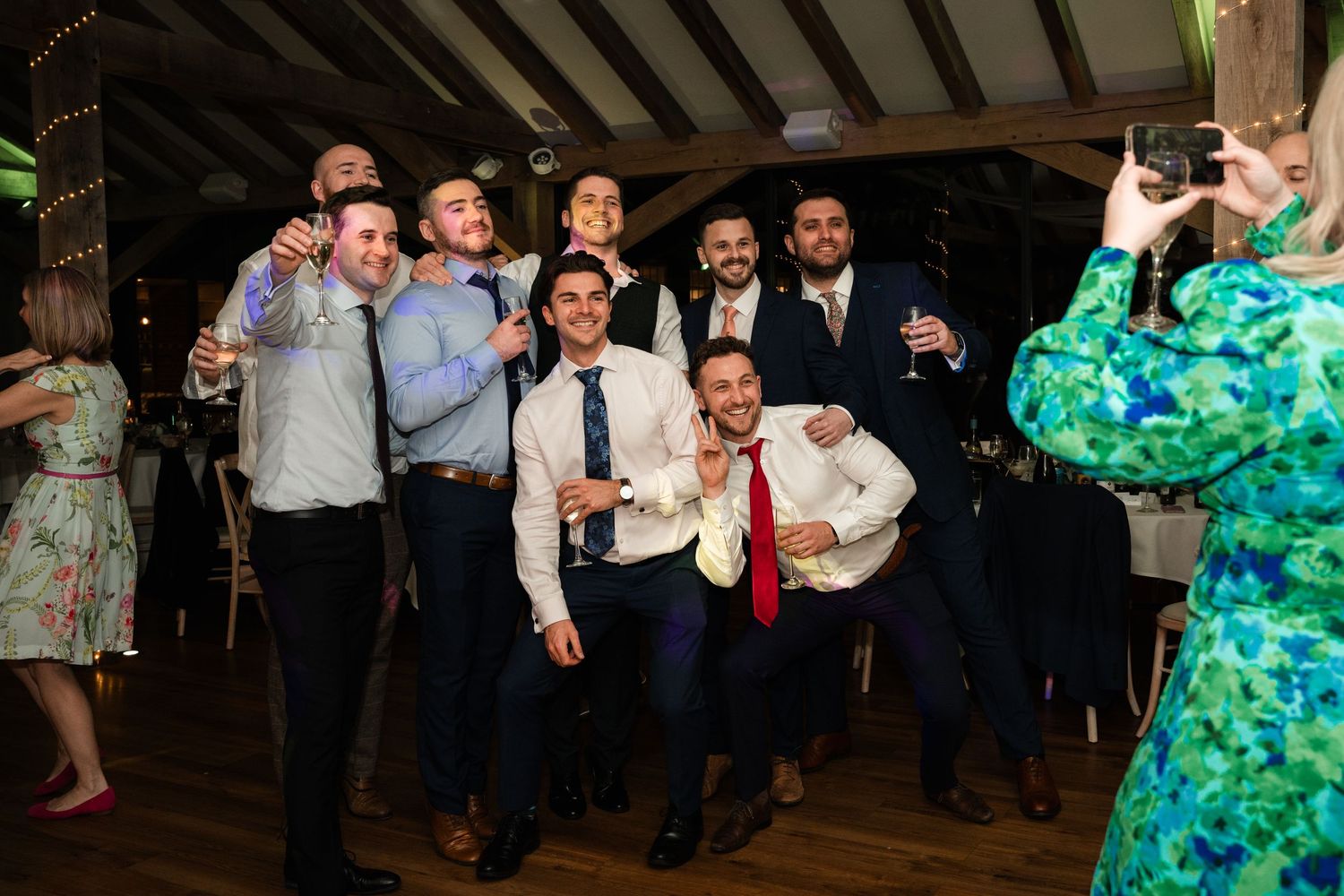 People dancing and celebrating at a lively wedding reception with a turquoise dress visible in the background.