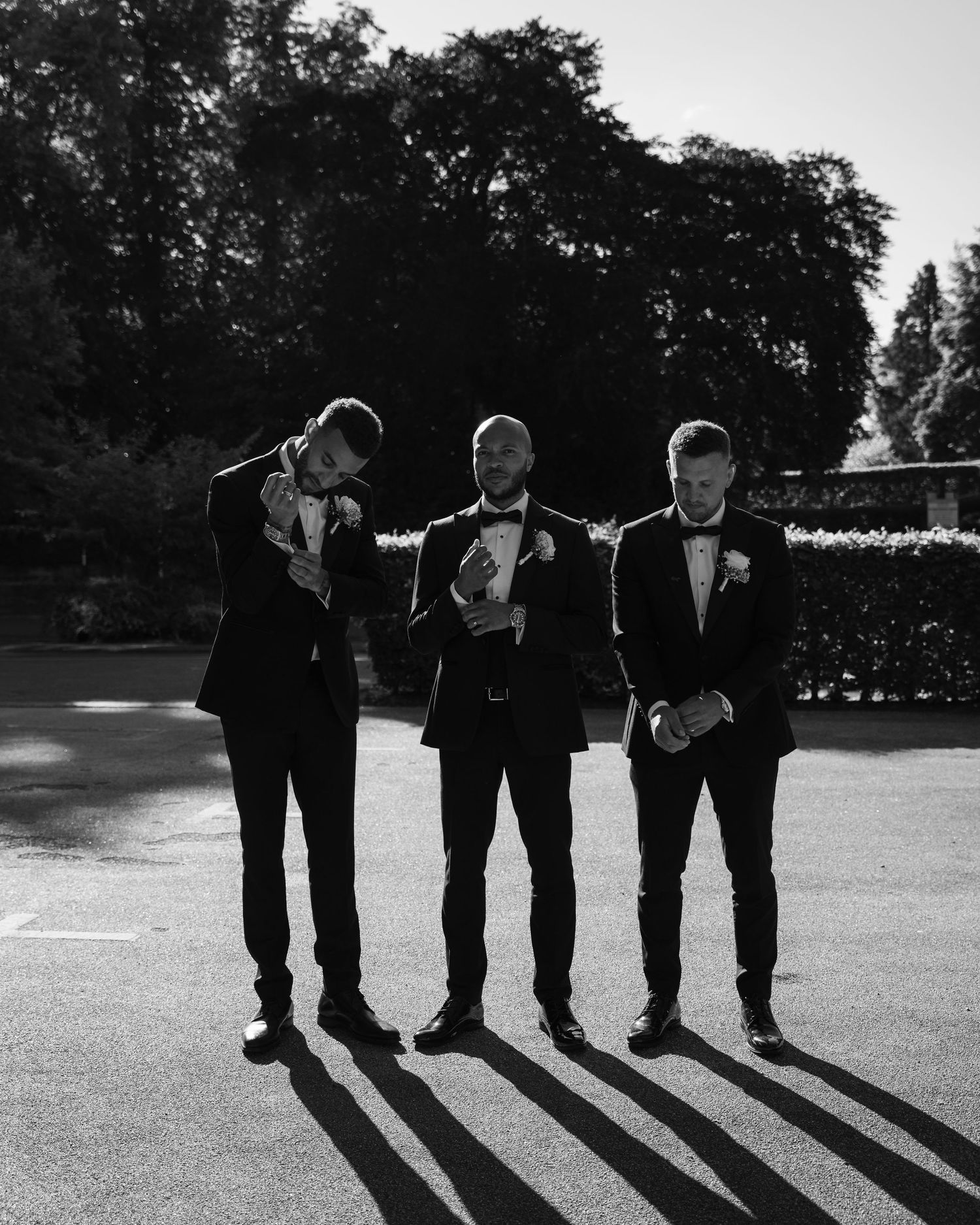 Four groomsmen cast long shadows while walking across an outdoor venue in a candid black and white photo series.