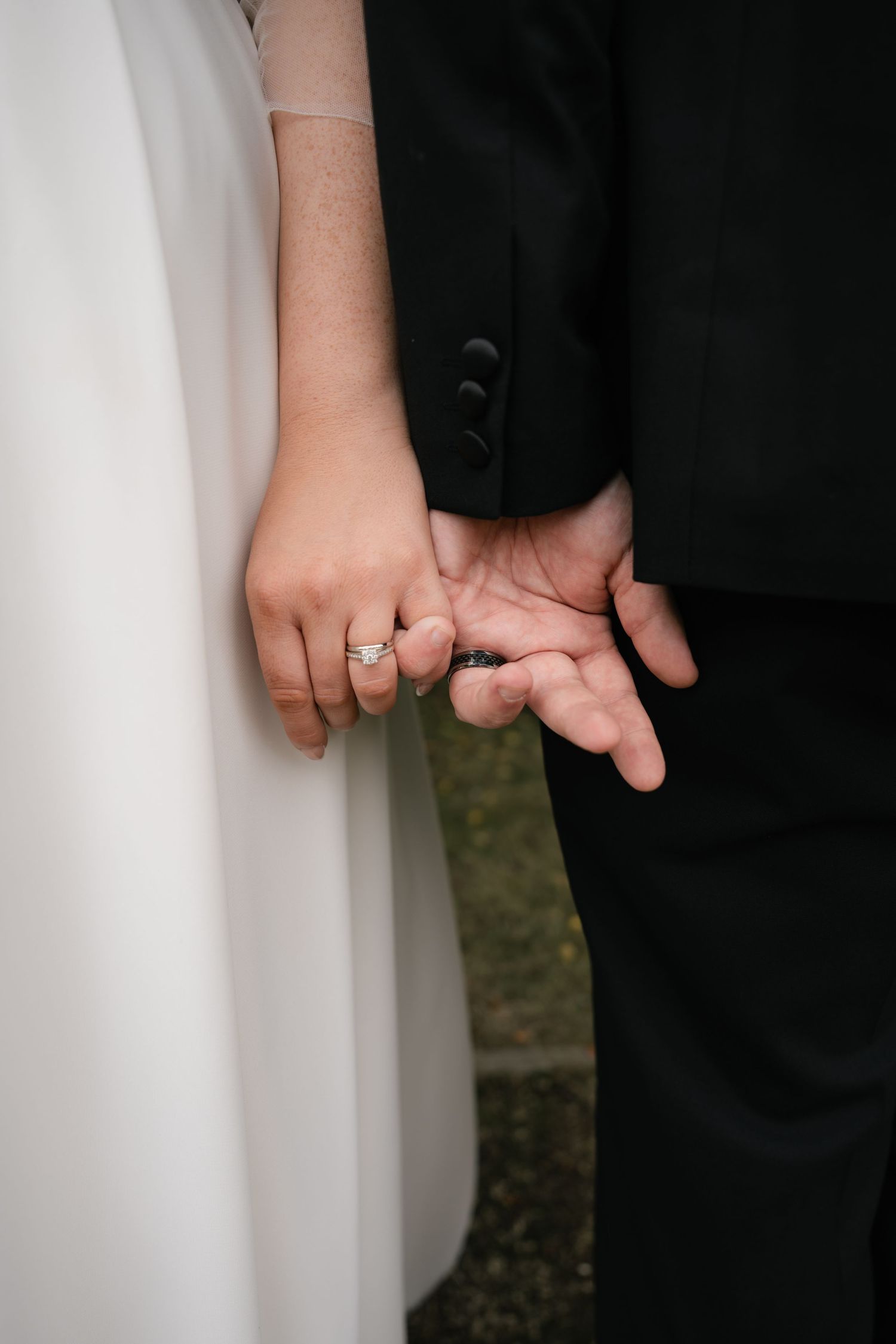 Close-up of a bride and groom holding hands showing wedding rings in an intimate moment.