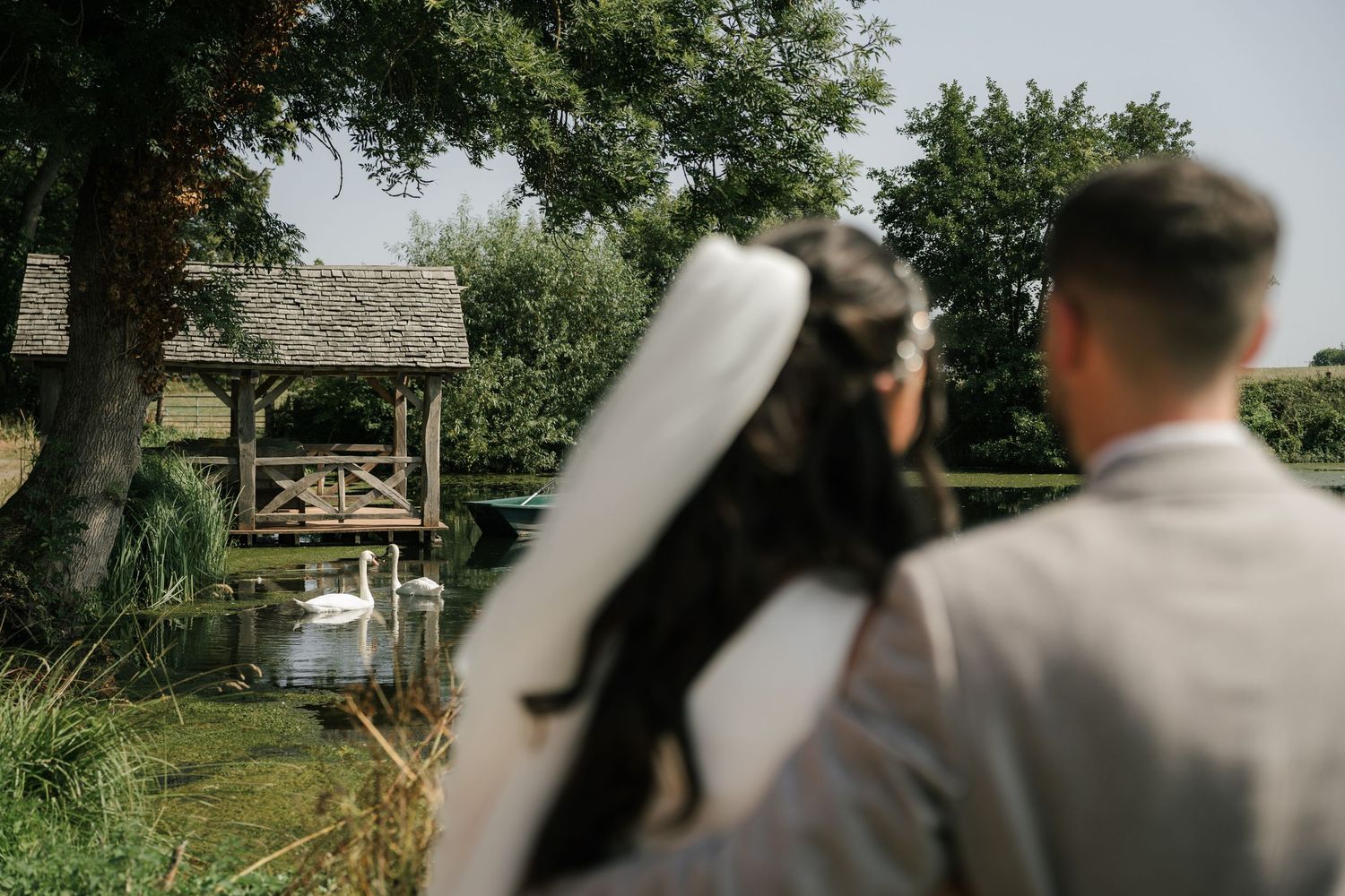 A scenic outdoor wedding ceremony setup with white chairs arranged in rows under green trees.