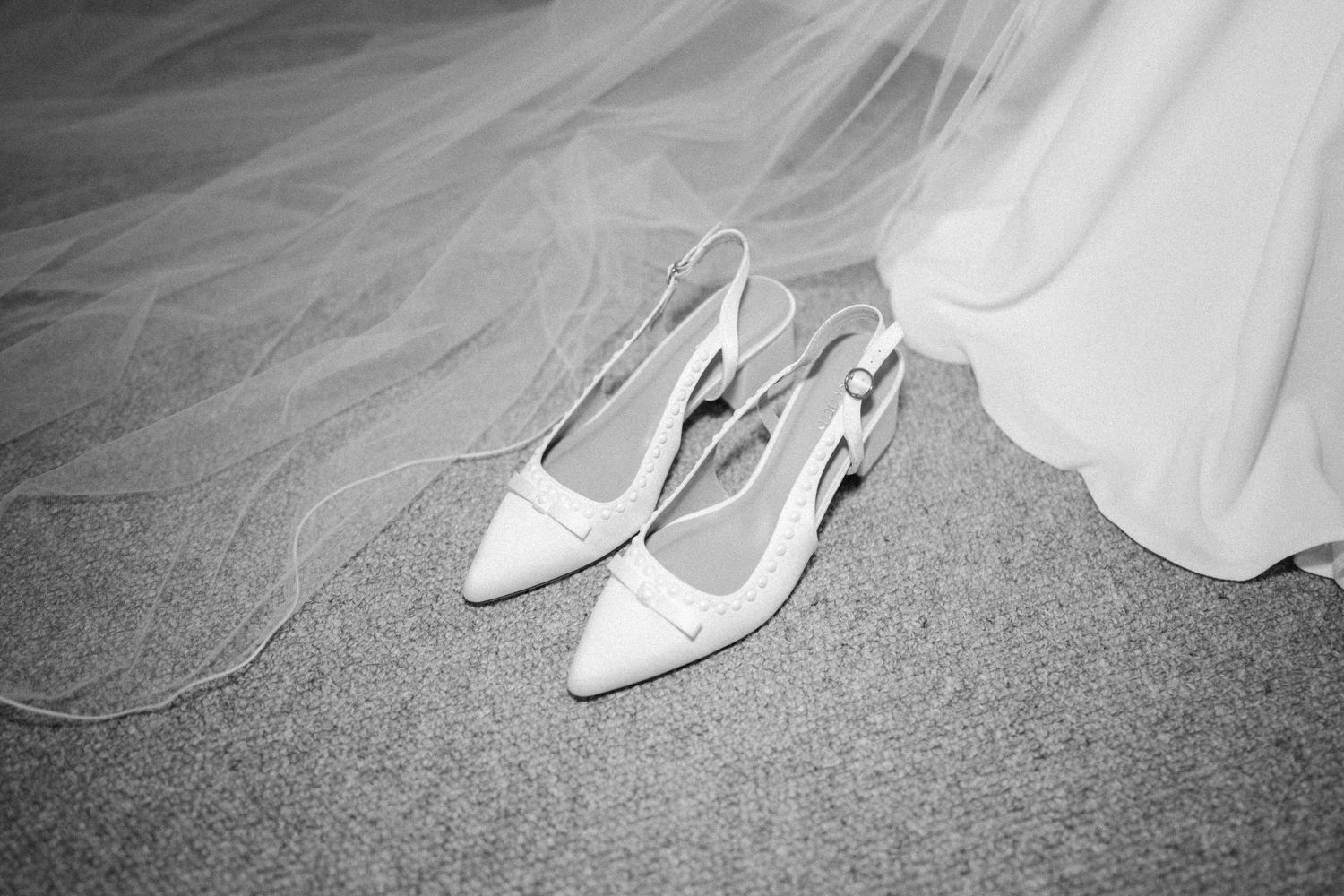 A row of white bridal shoes arranged on a gray carpet showing different angles and styles.