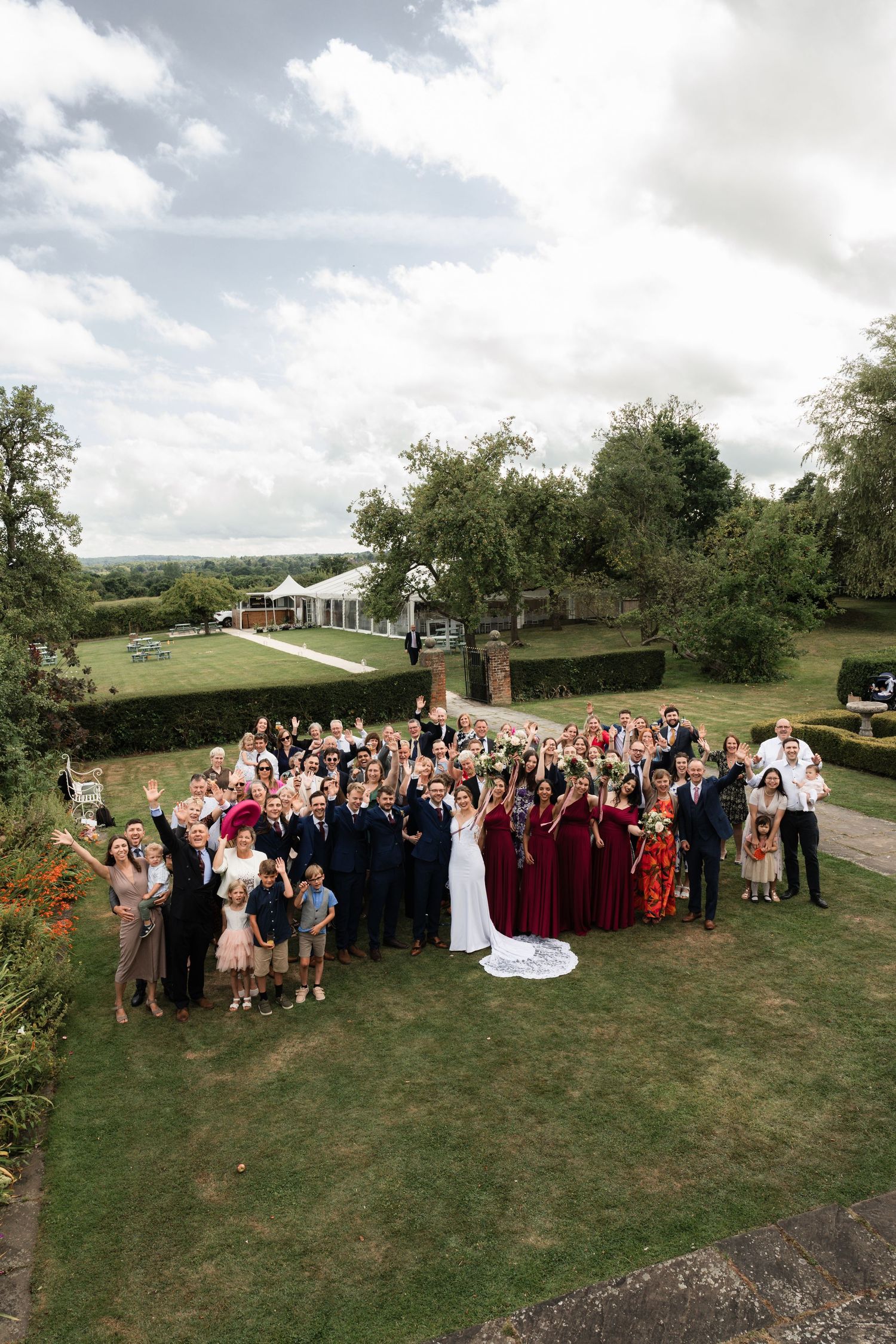 Large wedding party and guests gathered on a grassy hillside for group photos.