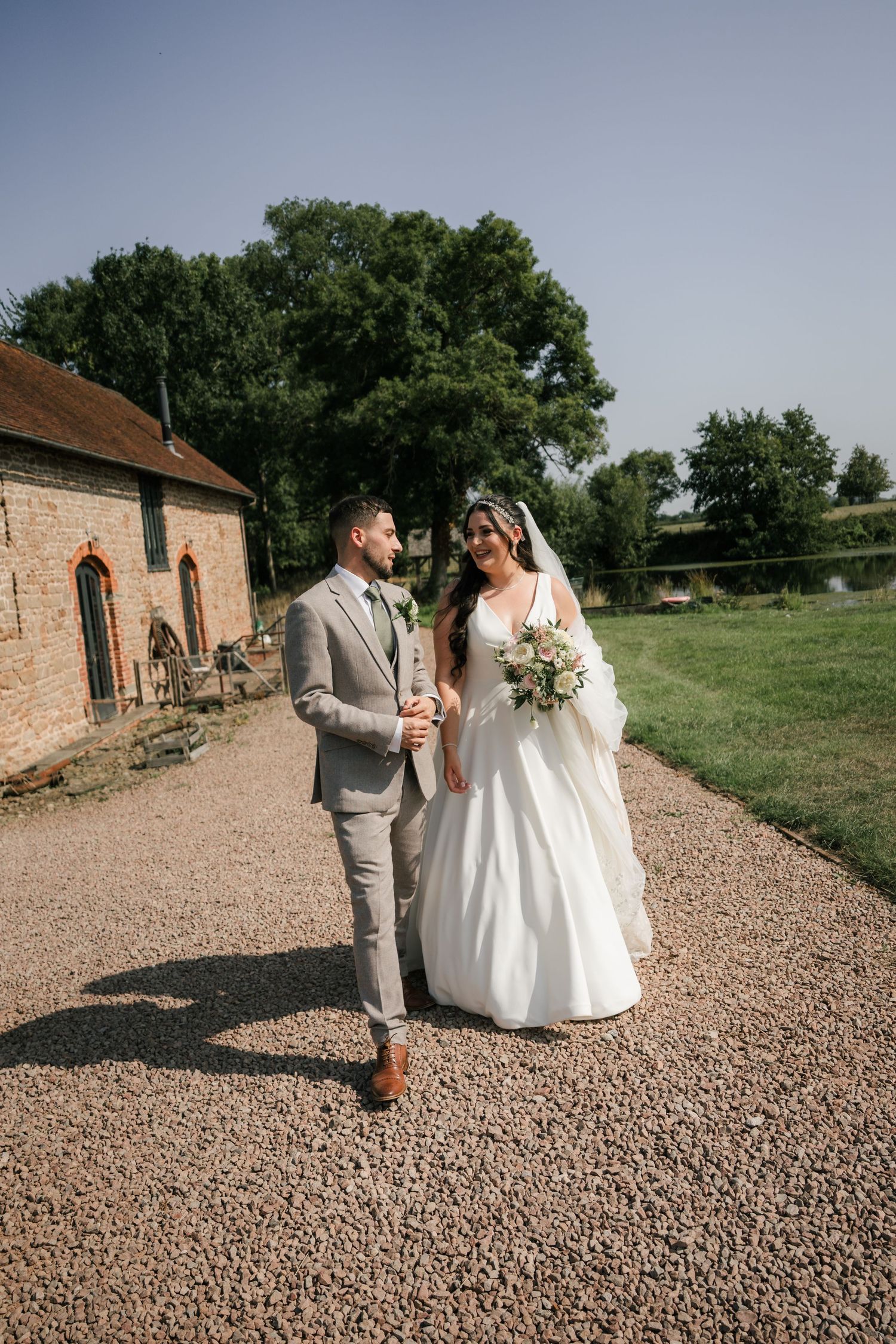 A couple shares a joyful moment together on a gravel path outside a rustic brick building on their wedding day.