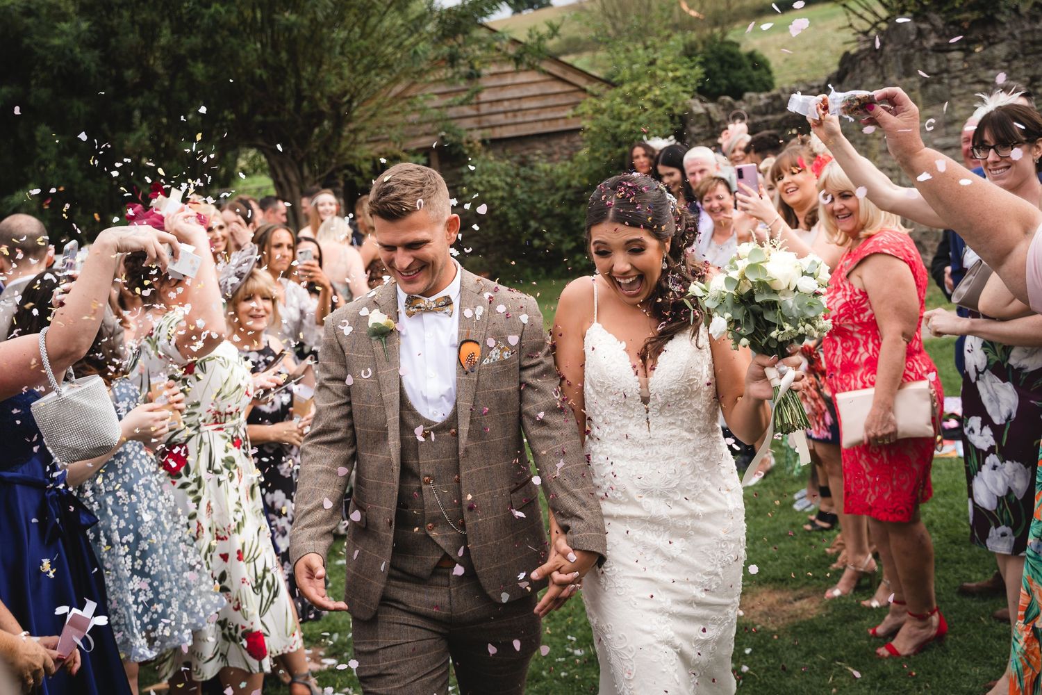 Wedding guests shower the newlyweds with white confetti during an outdoor celebration.