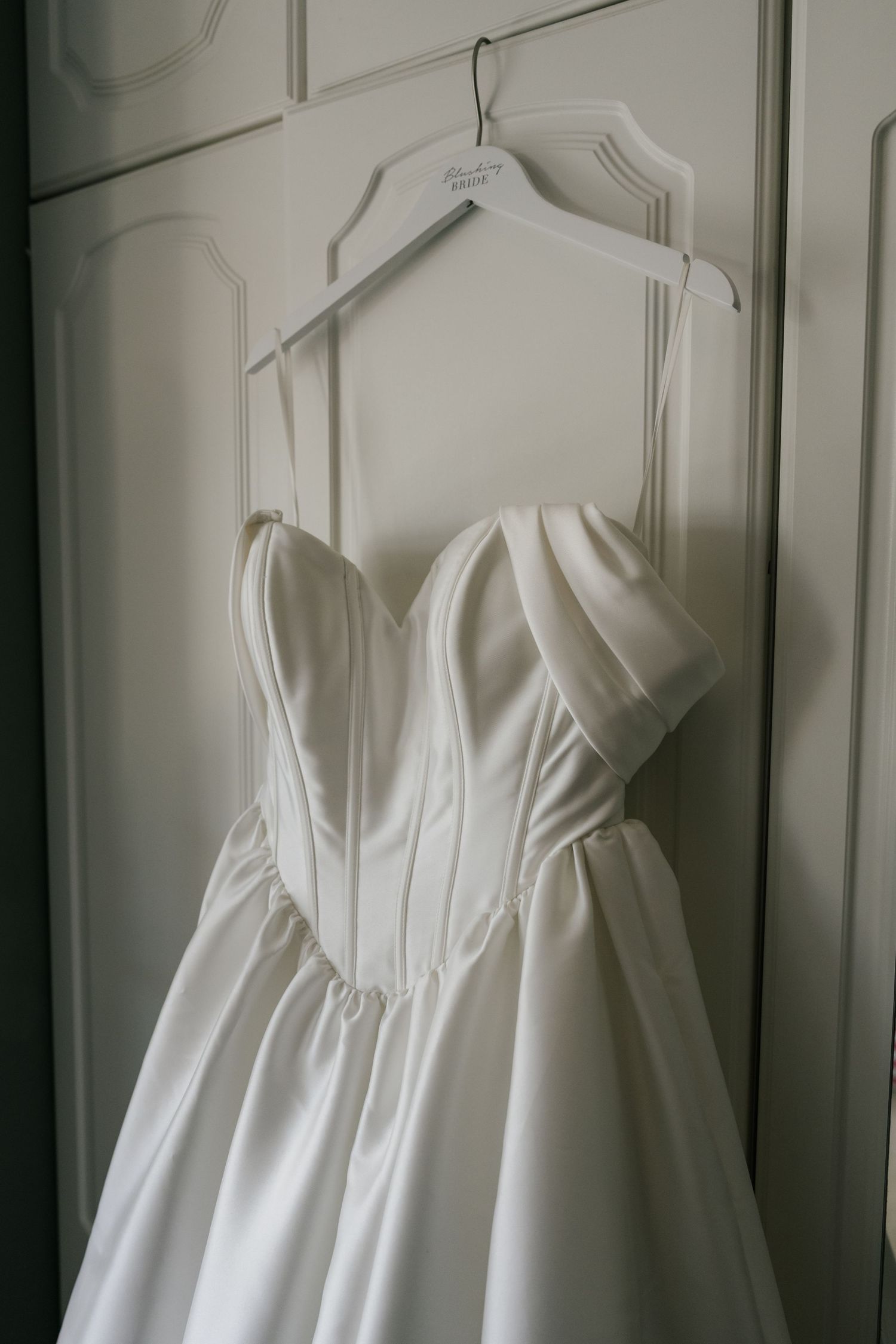 Elegant white satin wedding dress with sweetheart neckline and off-shoulder sleeves hanging on a white hanger.