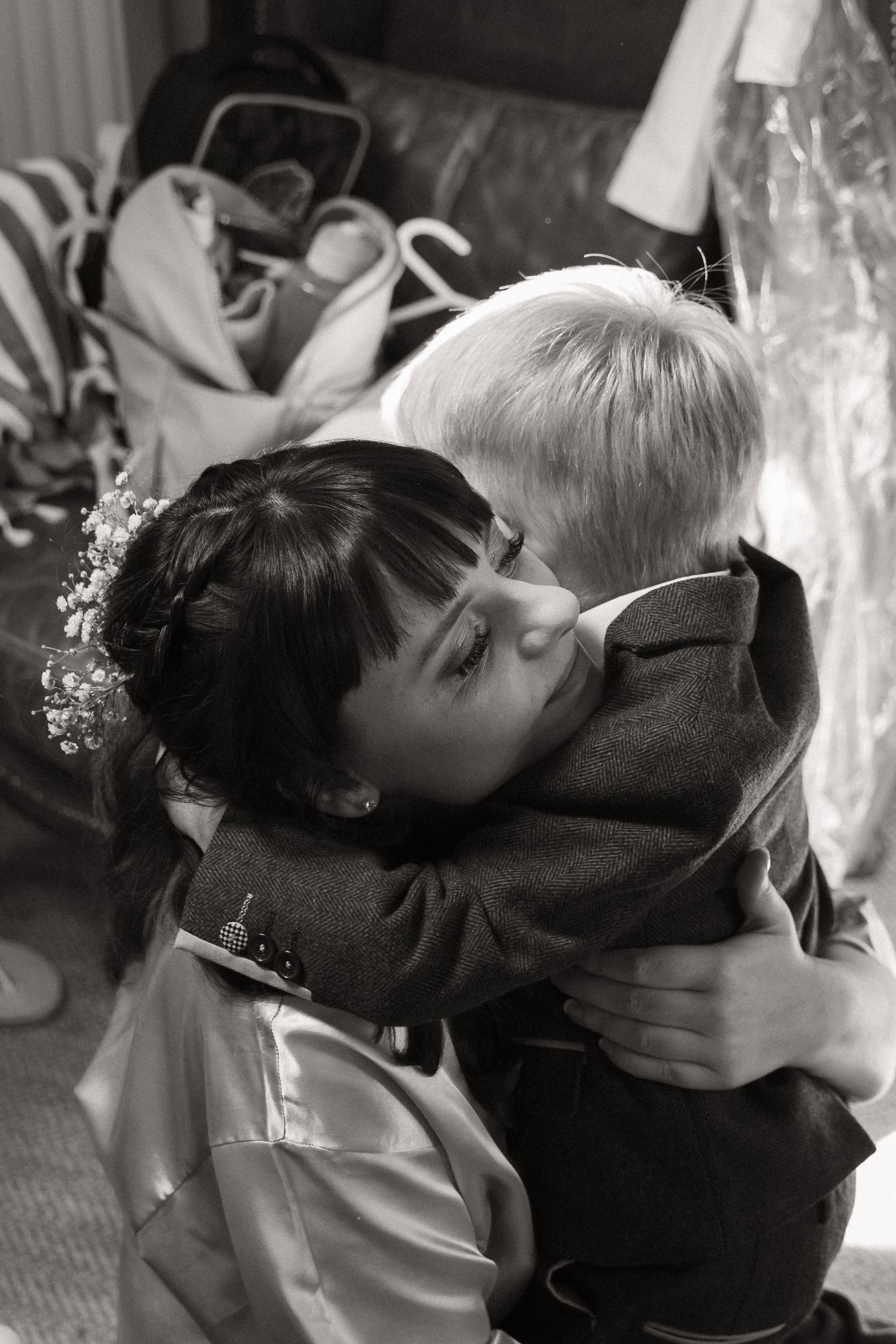 A tender black and white moment captured at a wedding as a bride in white embraces a small child in dark formal wear.