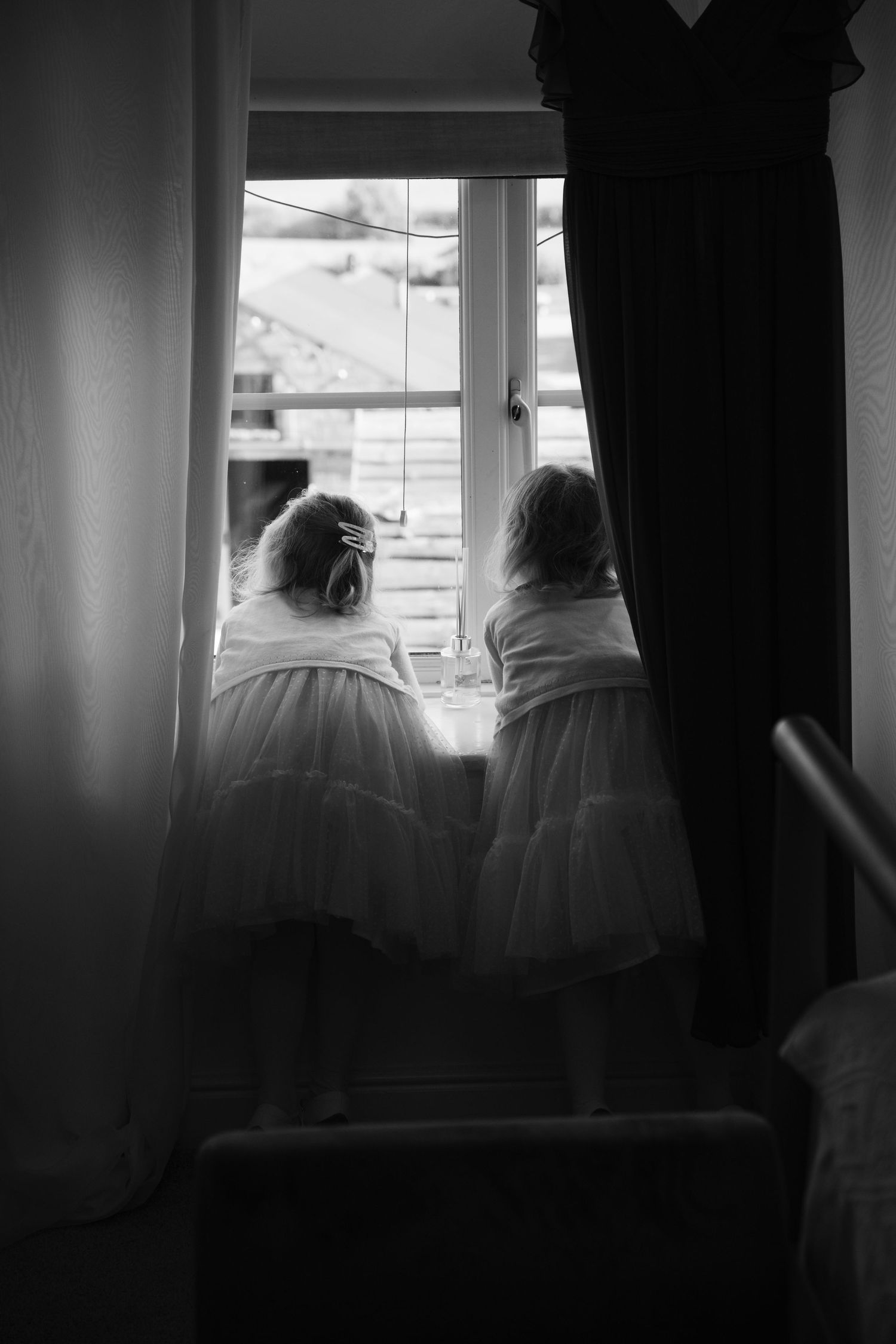 Two figures in white dresses sit by a window in a black and white photograph.