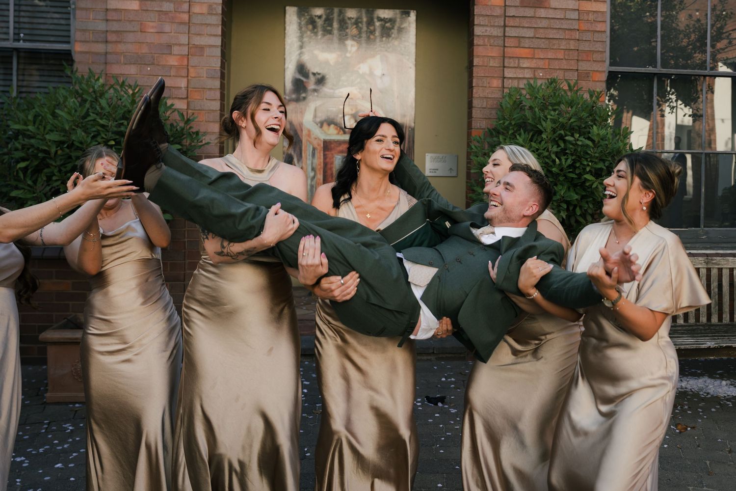 Bridesmaids in champagne dresses laughing and dancing together at a wedding celebration.