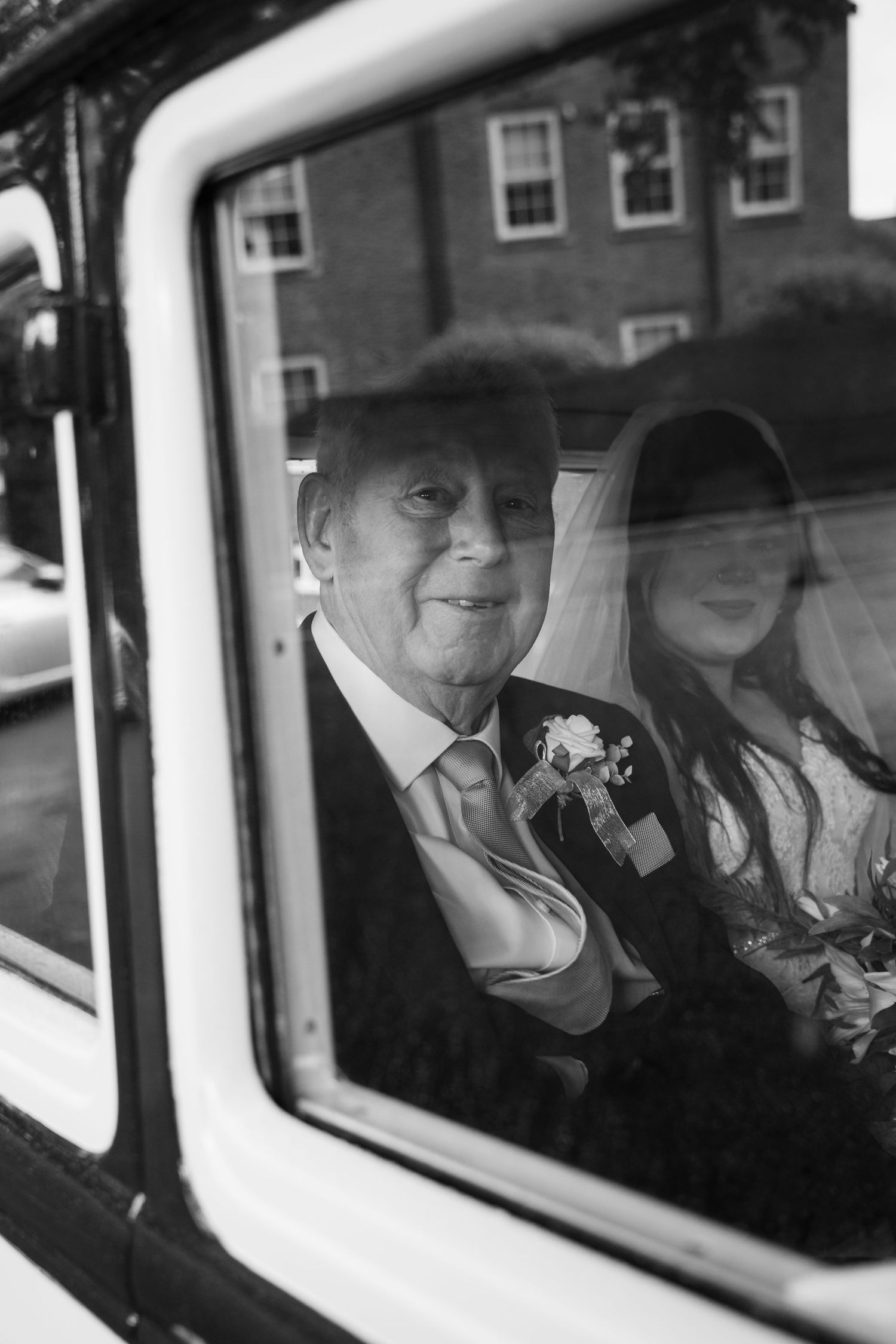 Black and white photo showing passengers through a car window on what appears to be a special occasion.