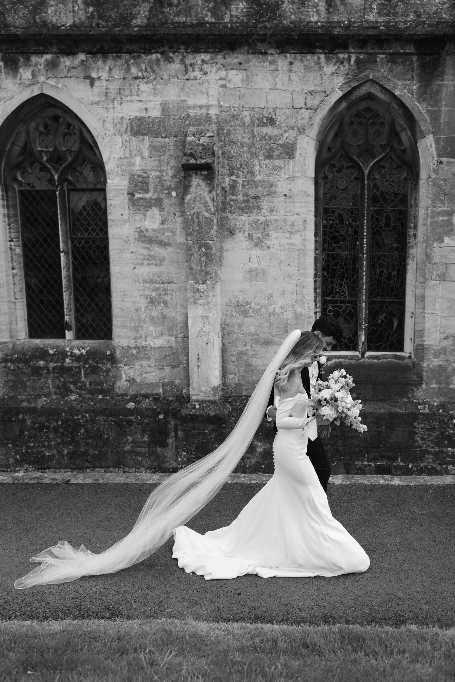 Four black and white wedding photos showing a bride's white dress and shoes against a stone church wall with gothic windows.