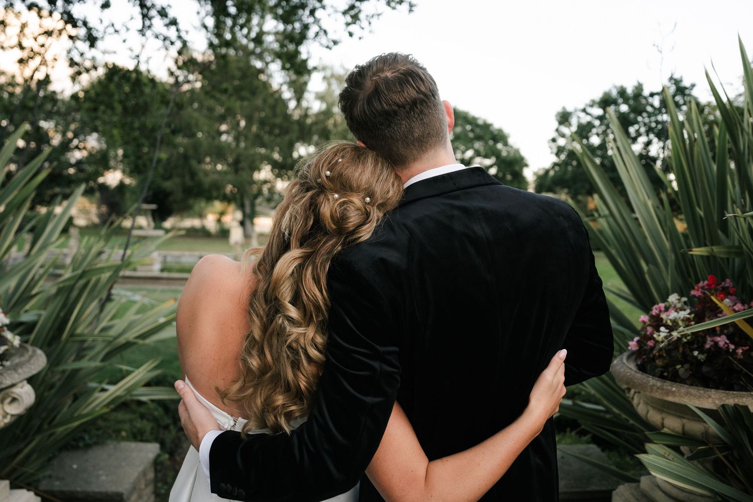 A couple embraces in a romantic outdoor setting surrounded by lush greenery and natural lighting.