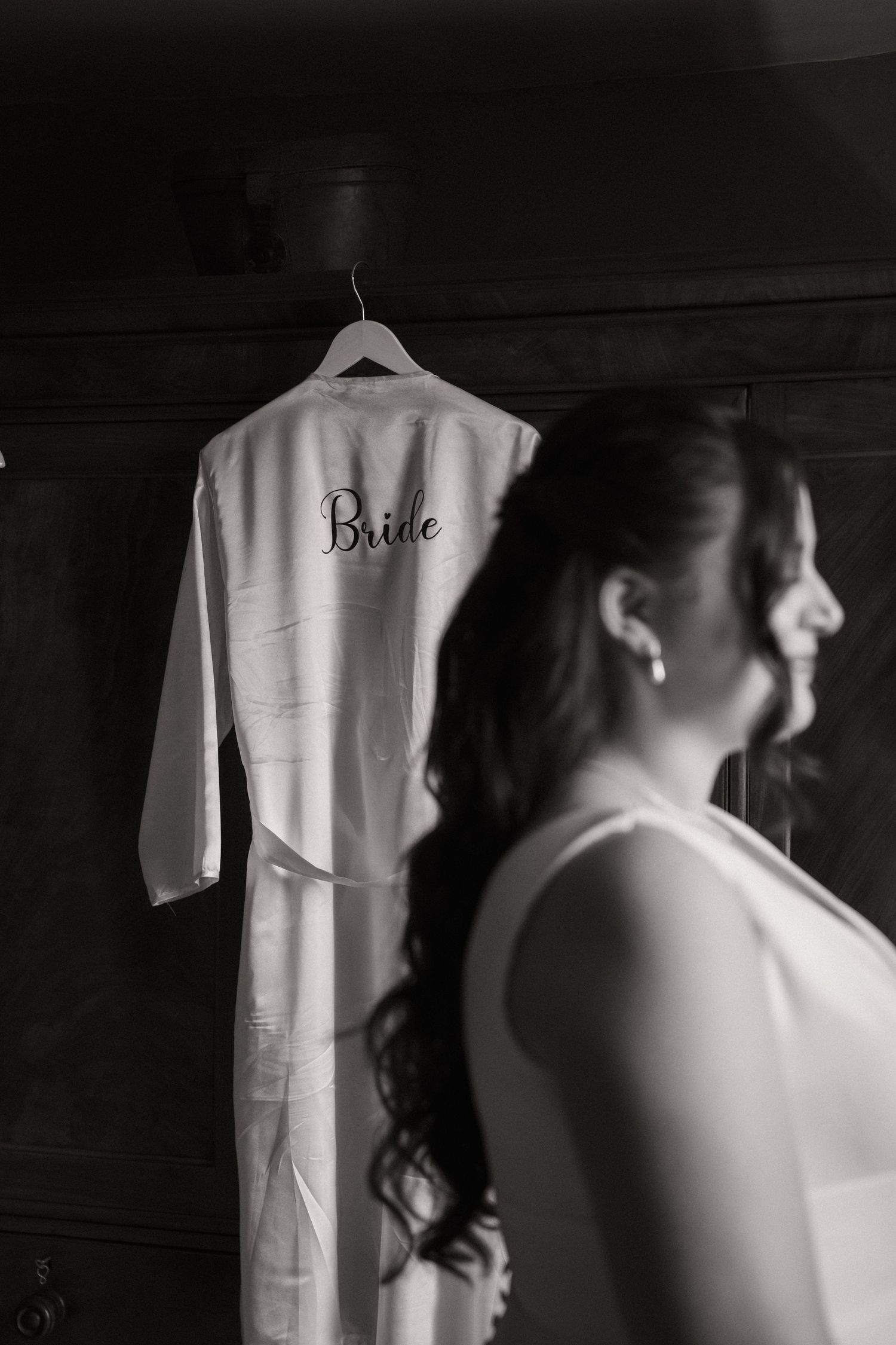 A white bridal robe hangs on display while a silhouetted figure stands in soft focus in the foreground.