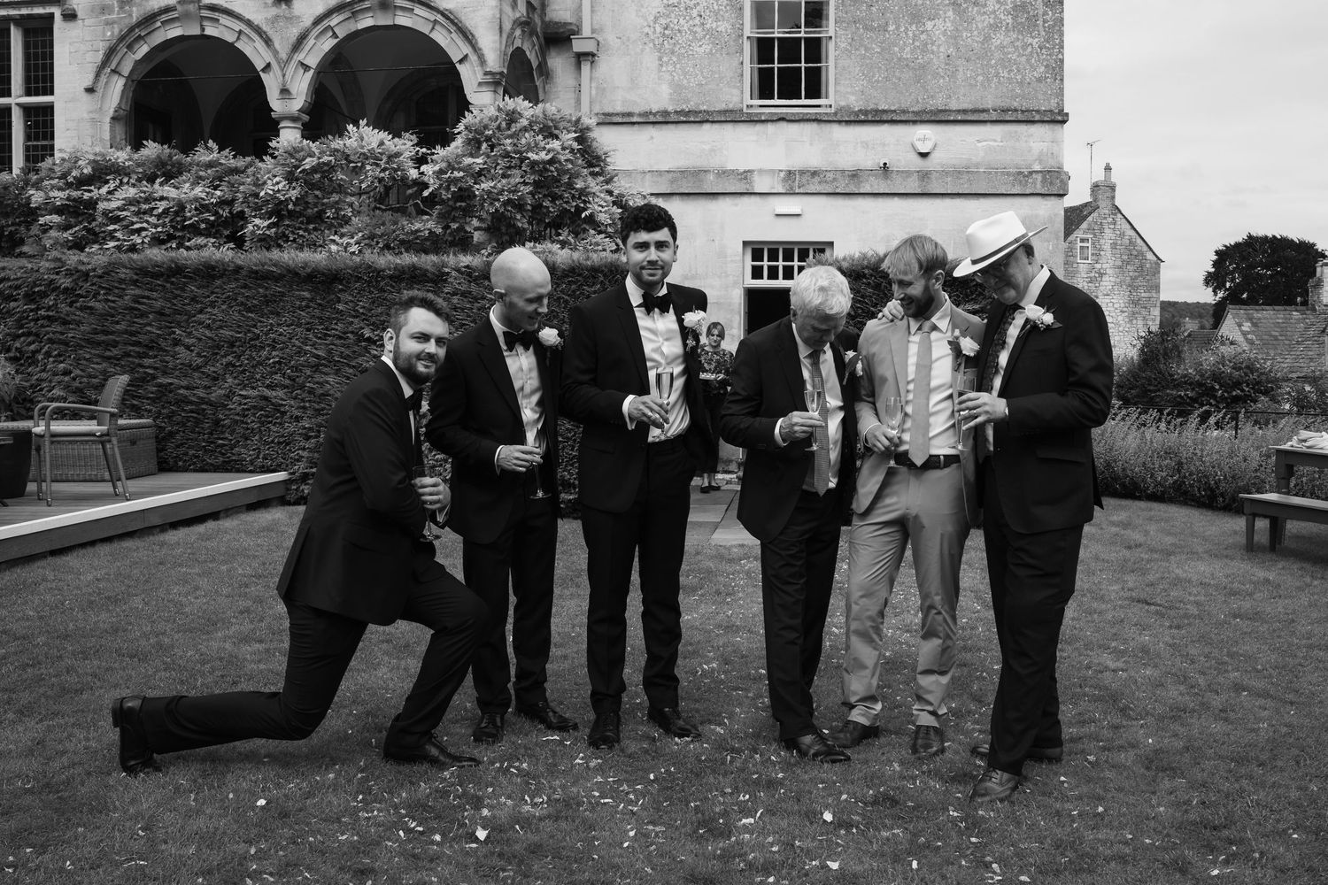 Black and white photo of wedding guests gathered on lawn outside historic building.