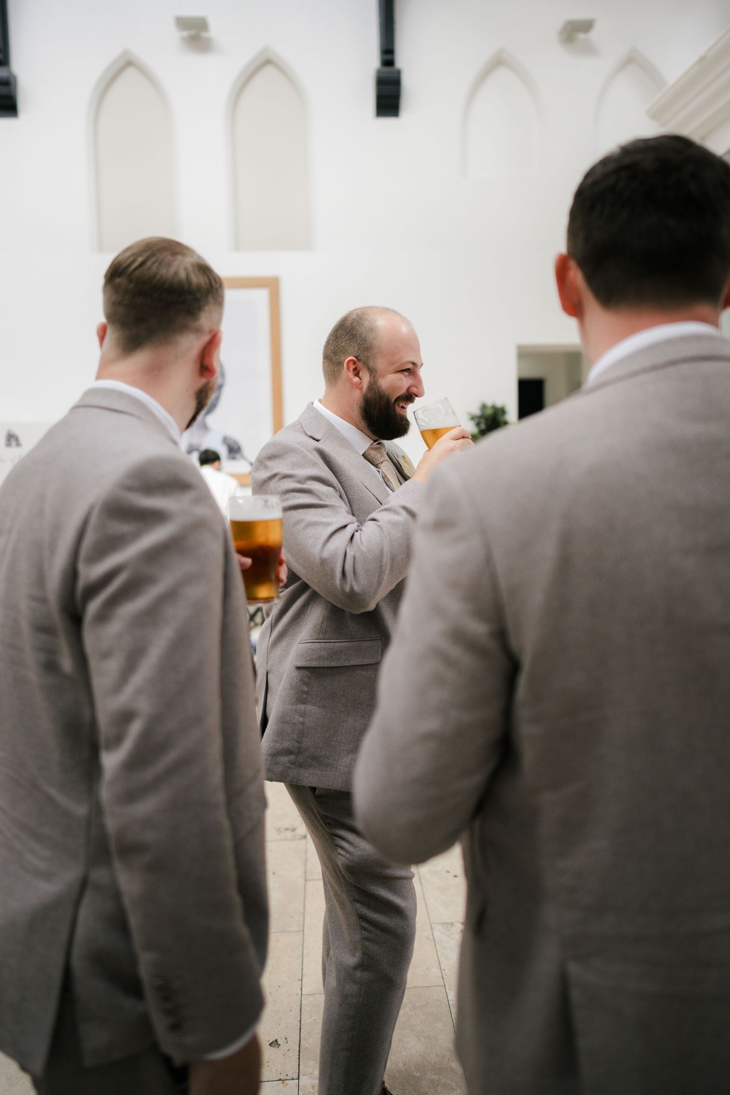 Groomsmen in matching gray suits share laughs and conversations at a wedding celebration.