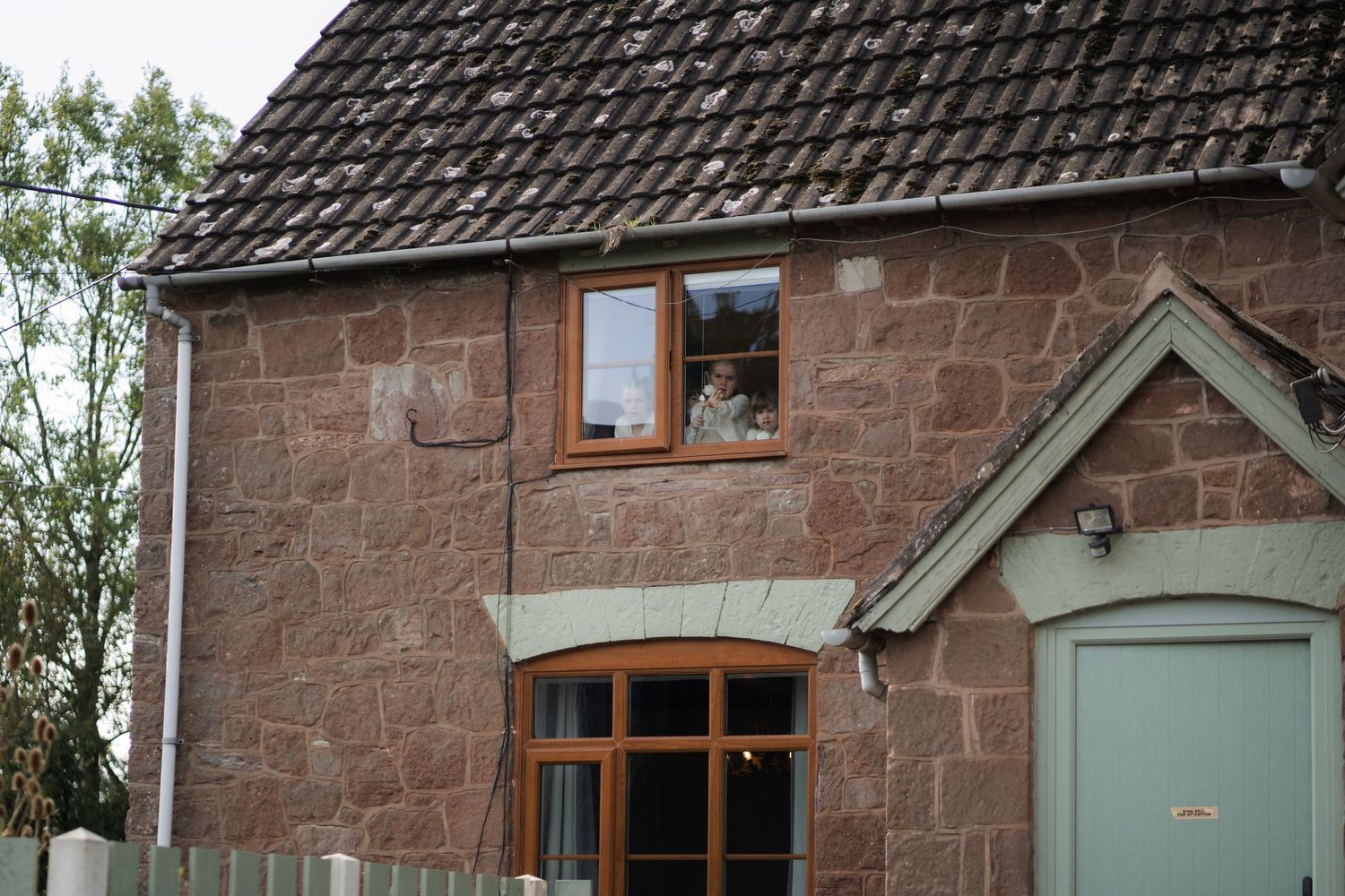 Traditional red sandstone cottage with wooden window frames and slate roof tiles in a rustic countryside setting.