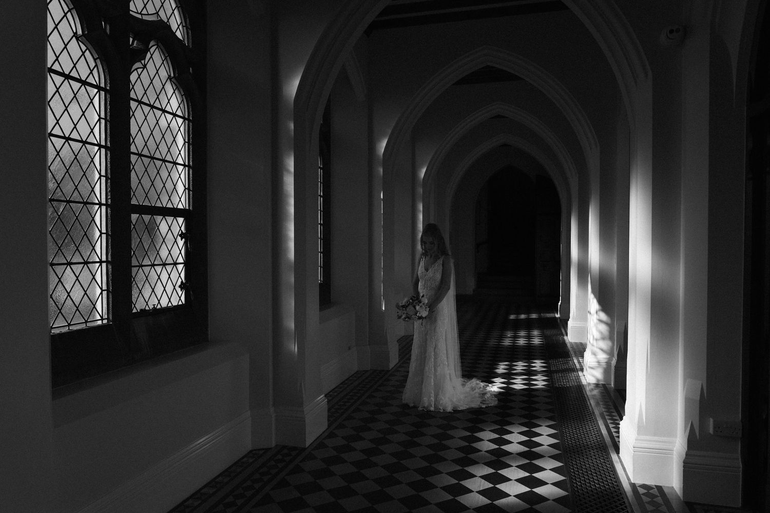 Gothic church corridor with black and white checkered floor and arched windows creates dramatic lighting and shadows.