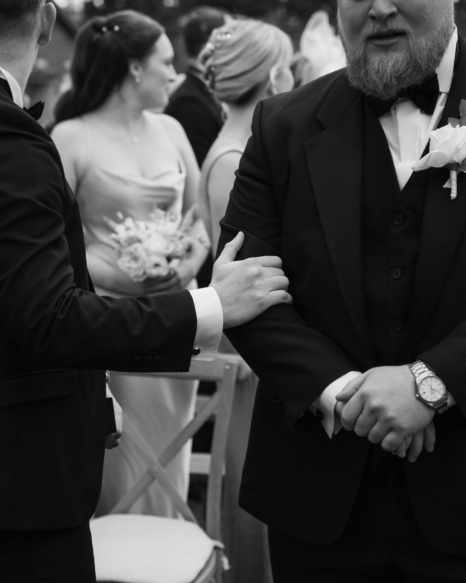 Black and white candid photo of wedding guests in formal attire during reception.