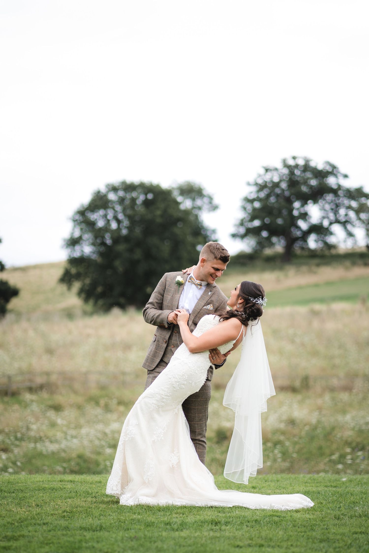 A couple shares a romantic dip pose on a grassy hillside during their wedding photoshoot.