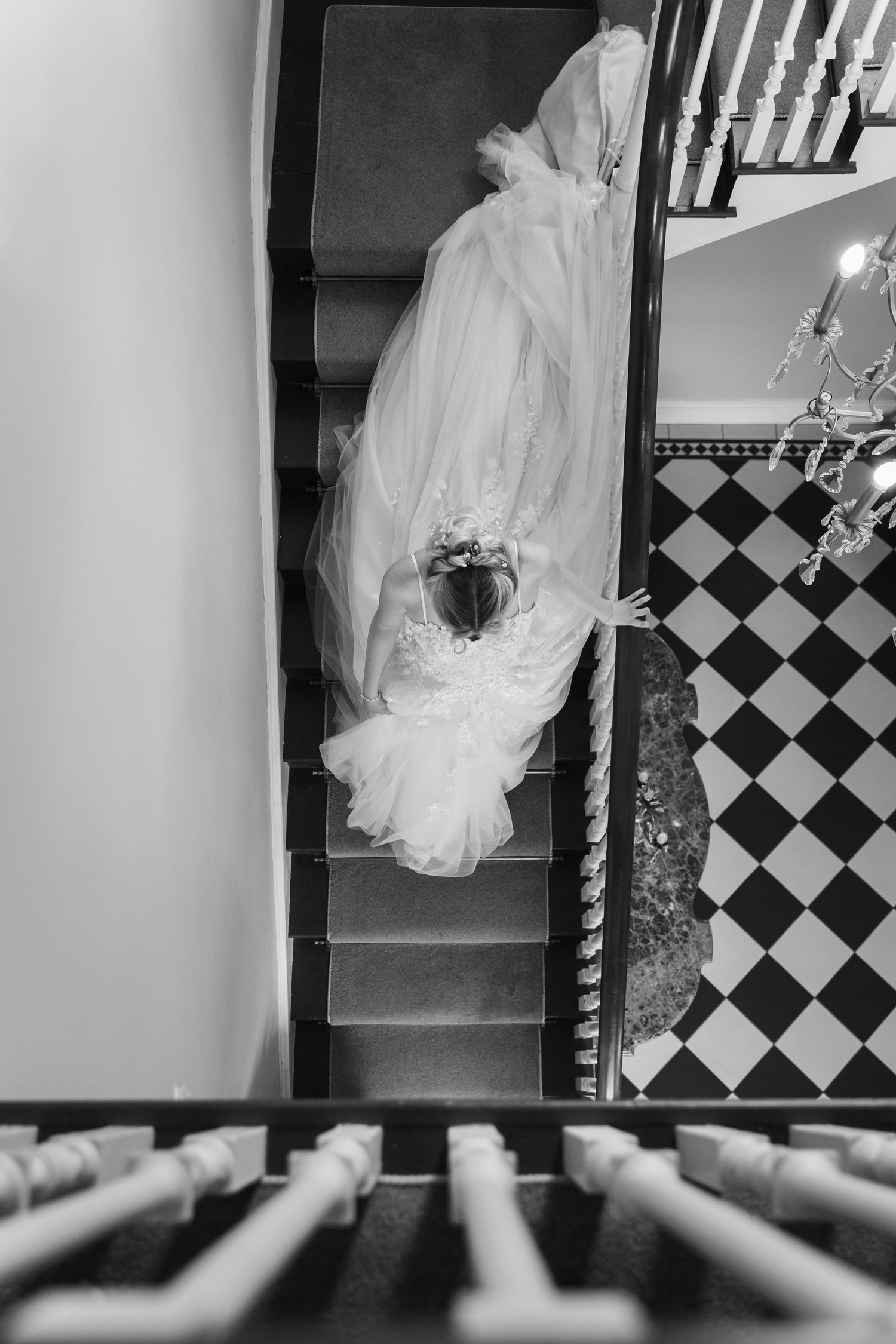 A flowing white wedding dress trails elegantly down a black and white checkered staircase.