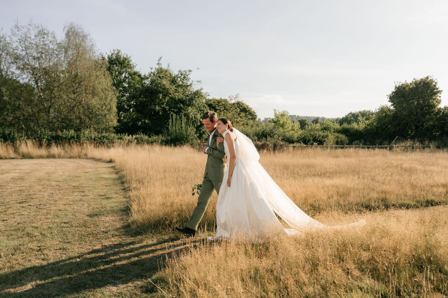 A romantic wedding photoshoot in a golden sunlit field with tall grass swaying in the breeze.