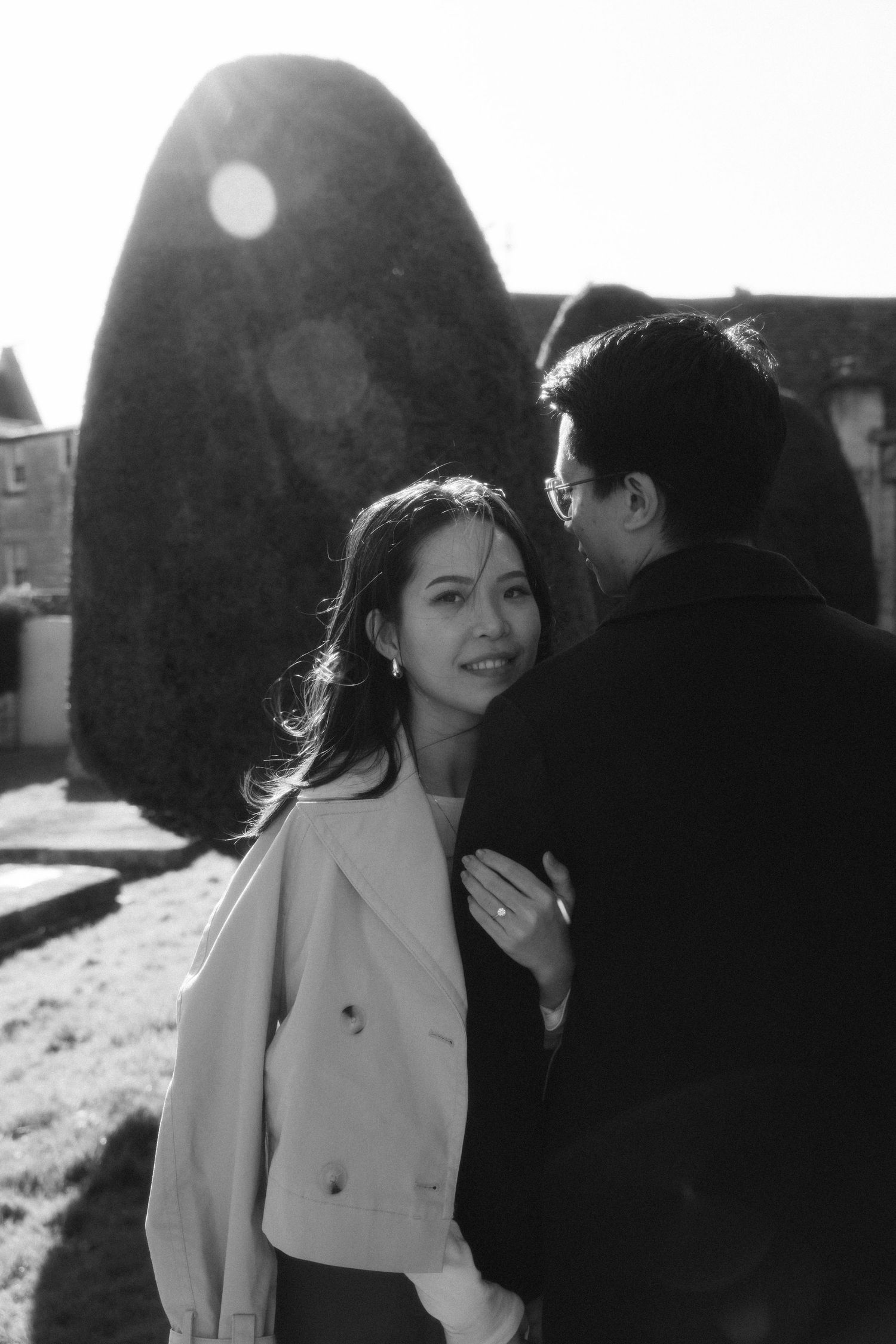 Romantic outdoor photoshoot featuring couple in winter coats against sunlit backdrop.