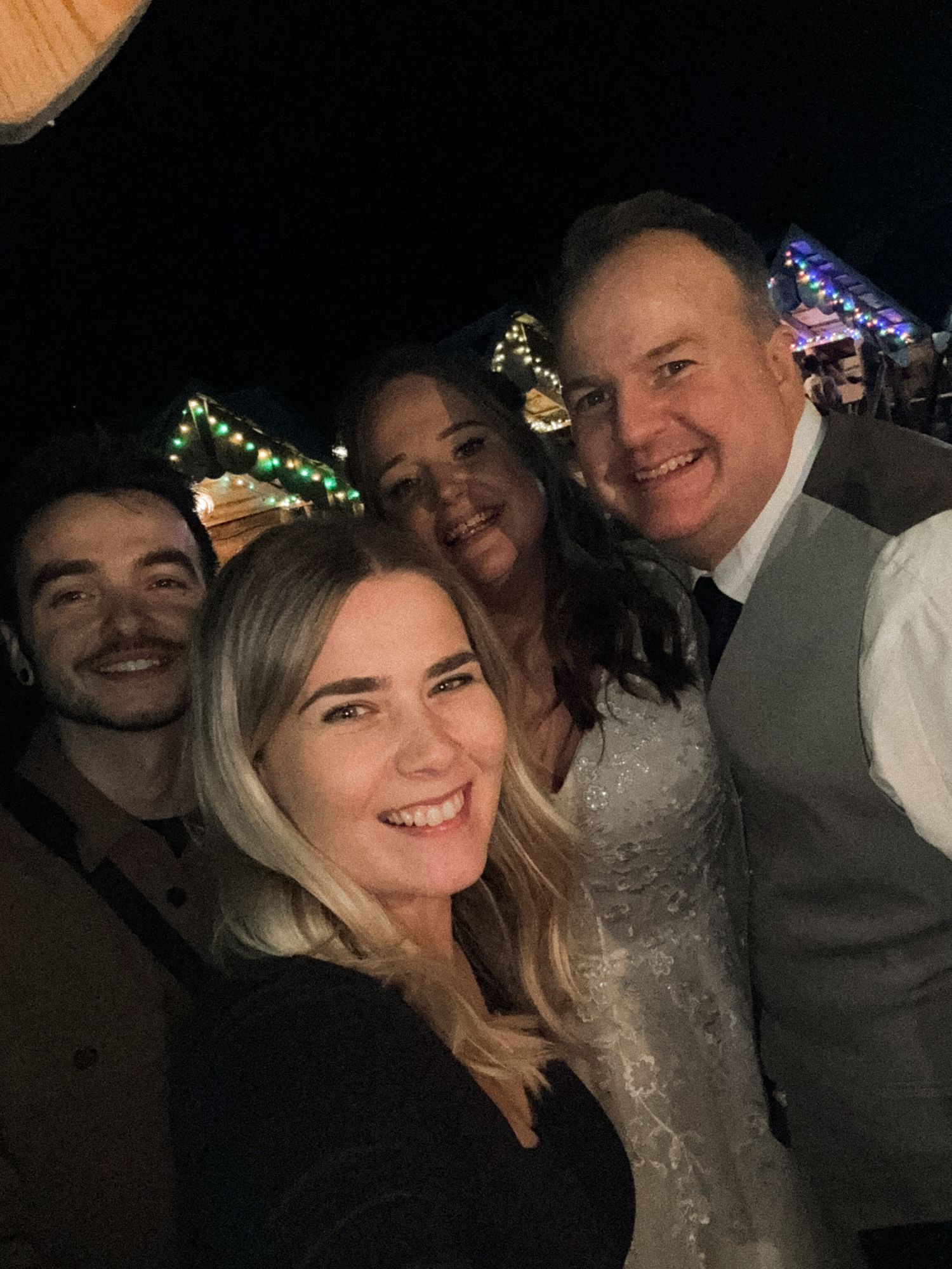 A group of people smiling together in a dark setting with colorful lights visible in the background.